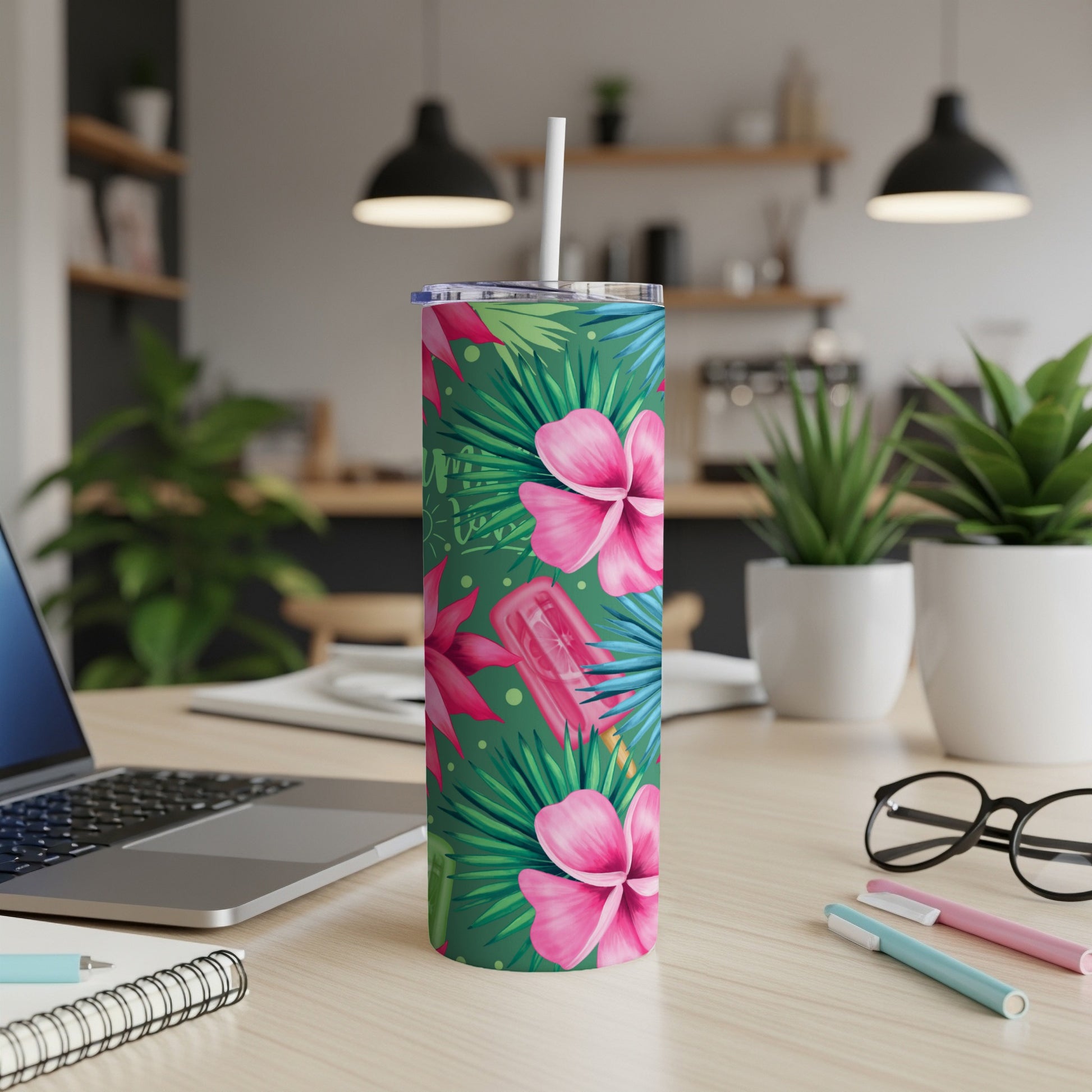 Green tumbler with pink flowers and palm leaves, on a desk with a laptop.