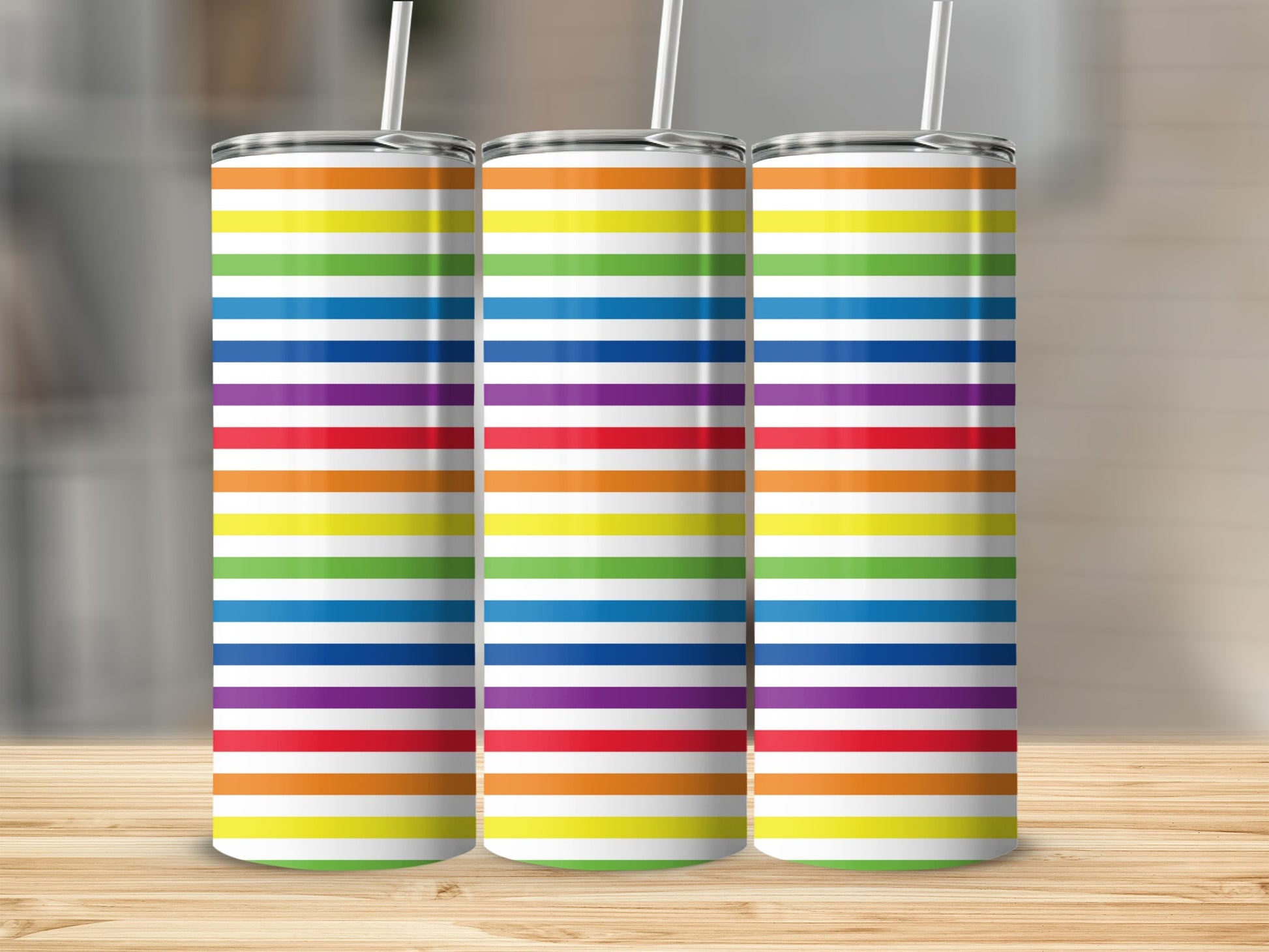 Three tall tumblers with rainbow stripe patterns stand side-by-side on a wooden surface.
