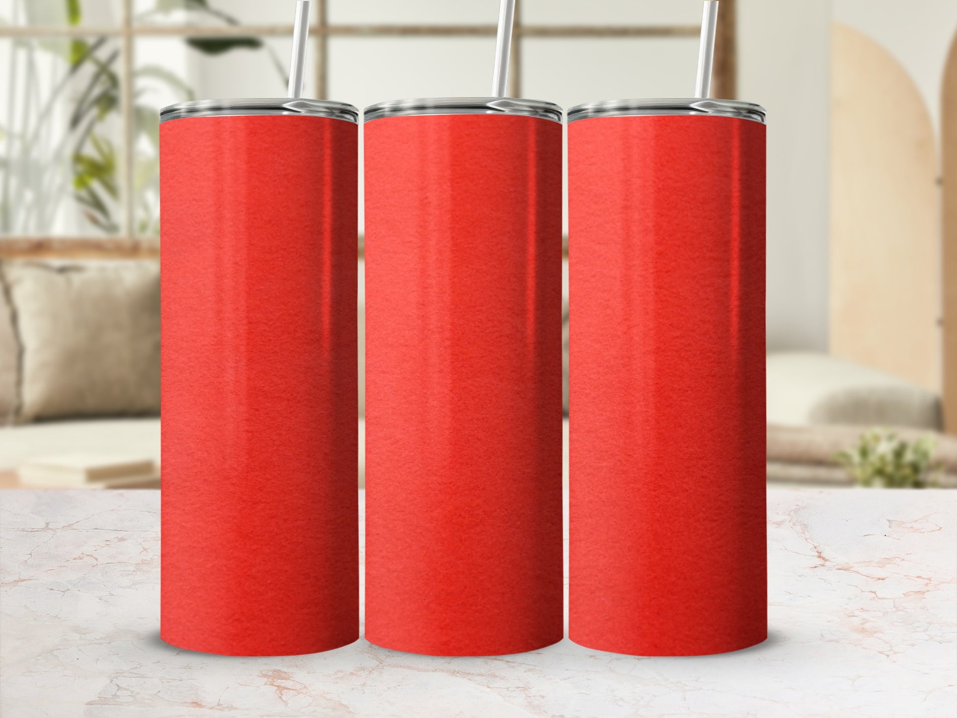 Three red tumblers with straws on a marble countertop, with a blurred background.