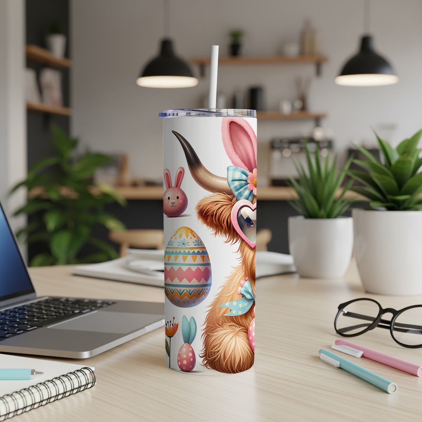 Easter cow tumbler with hearts, eggs, and flowers, on a desk.
