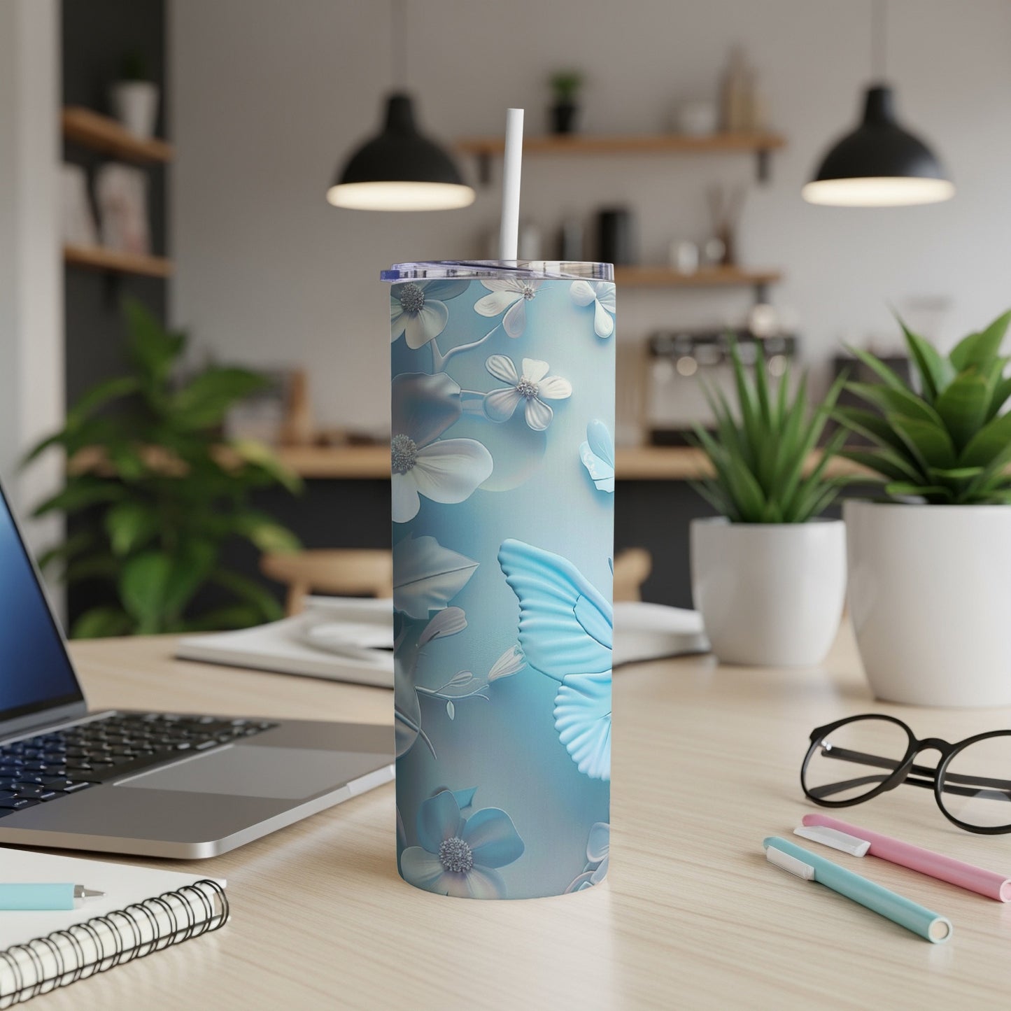 Blue butterfly and floral pattern on a tall tumbler with a straw, on a desk.