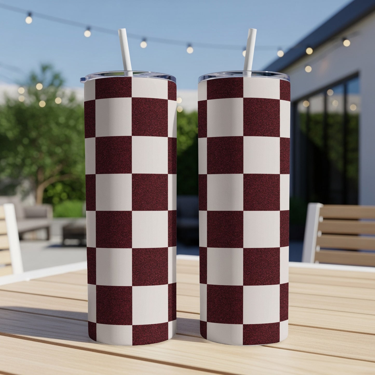 Two tumblers with a maroon and white checkered pattern sit on a wooden table outdoors.