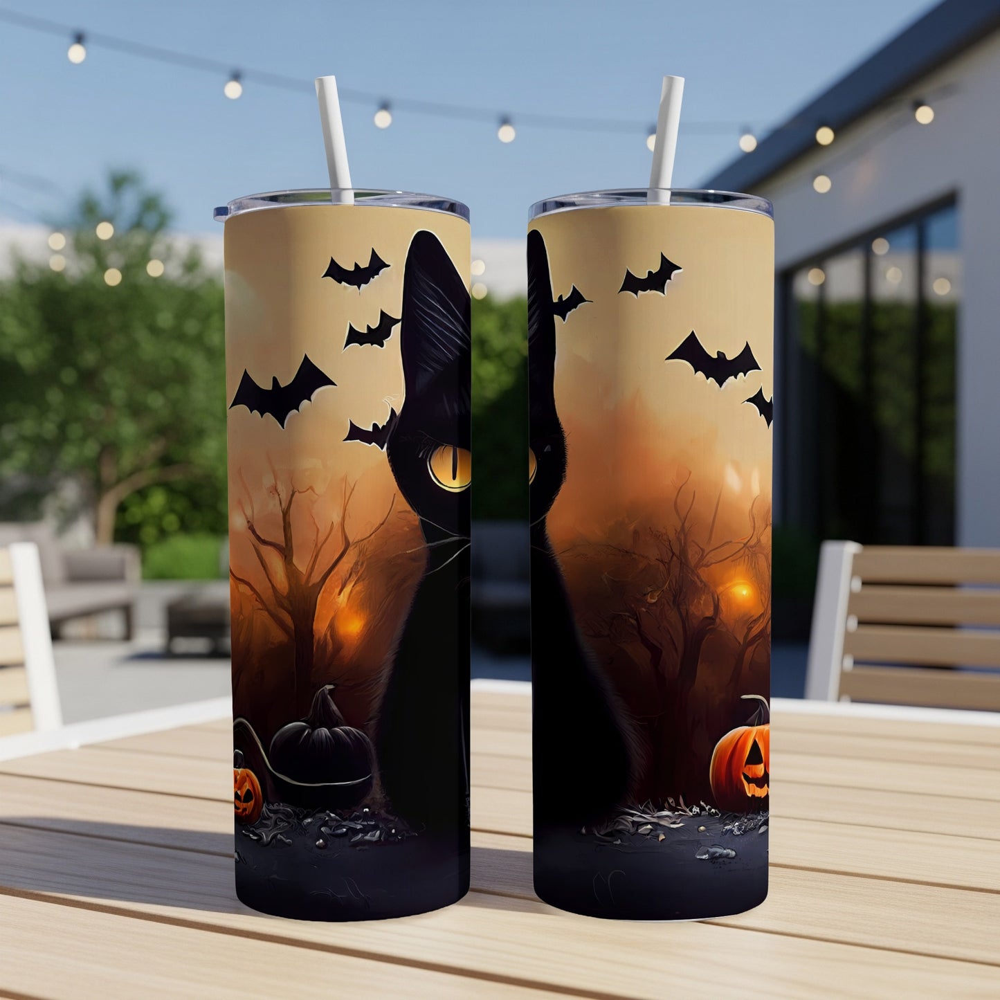 Two Halloween-themed tumblers with a black cat and bats on a wooden table outdoors.