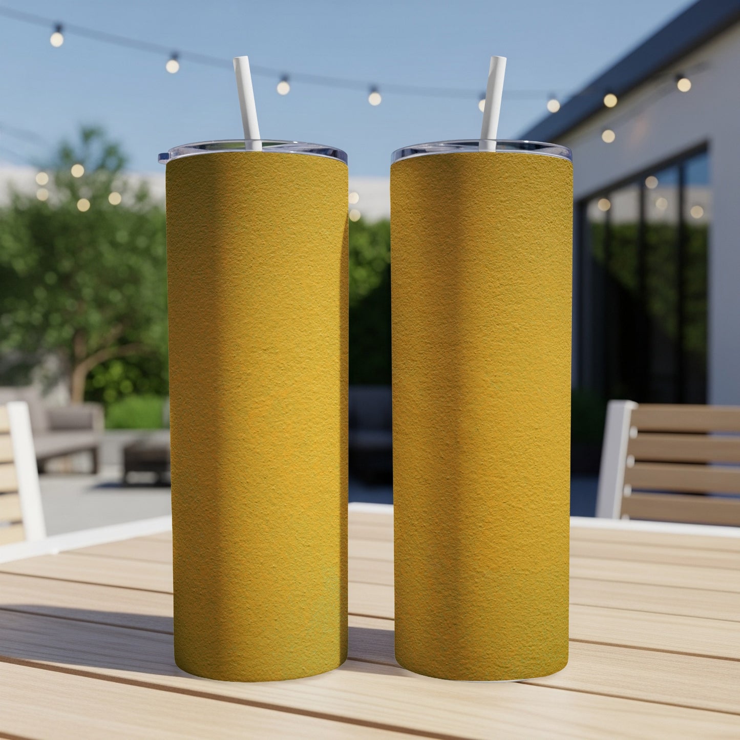 Two yellow textured tumblers with straws sit on a table outdoors.