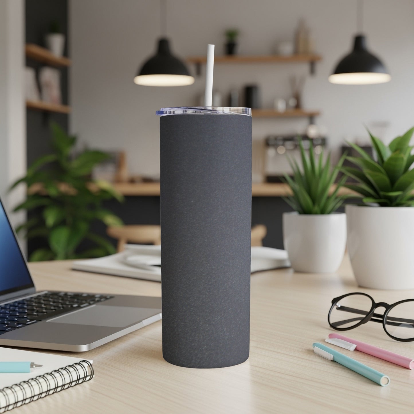 Charcoal grey tumbler with white straw on a desk next to a laptop.