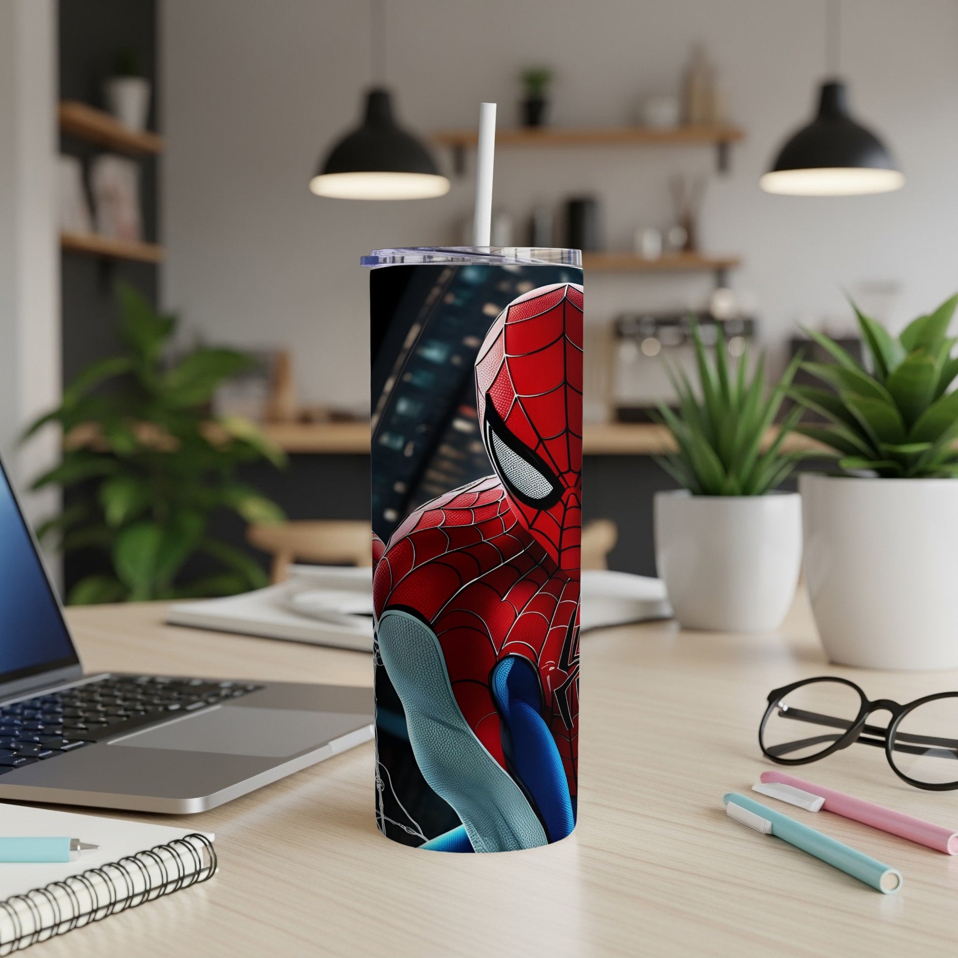 Spider-Man tumbler with city background, on desk with laptop and pens.