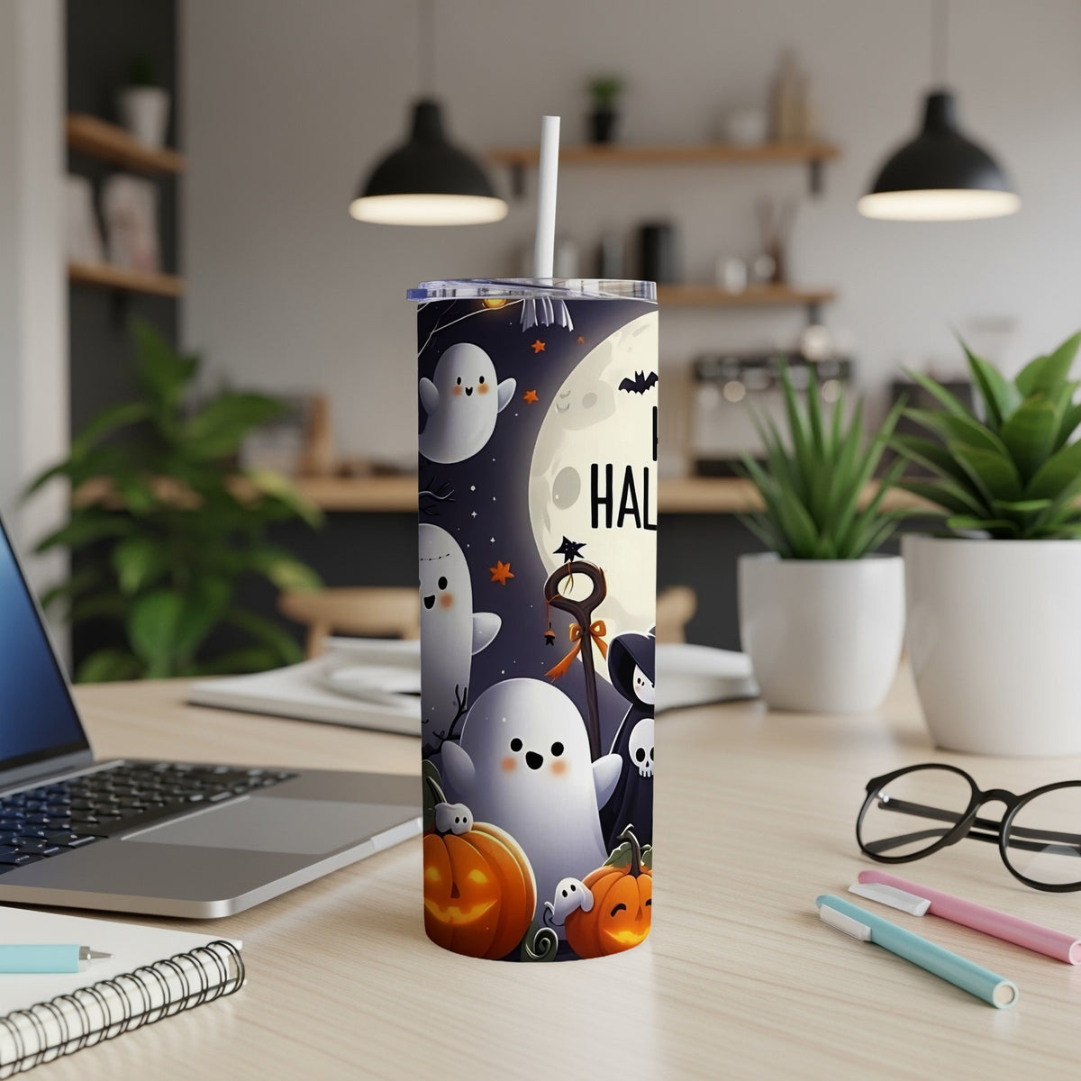 Halloween tumbler with ghosts, pumpkins, and a full moon on a desk.