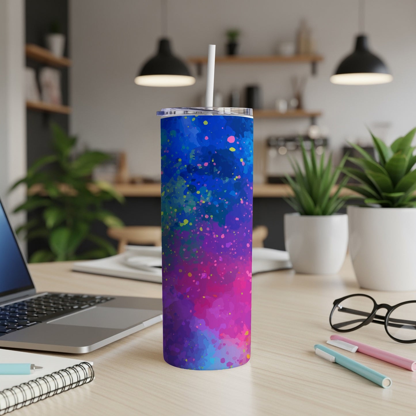 Tumbler with colorful abstract paint splatter design and white straw on a desk.