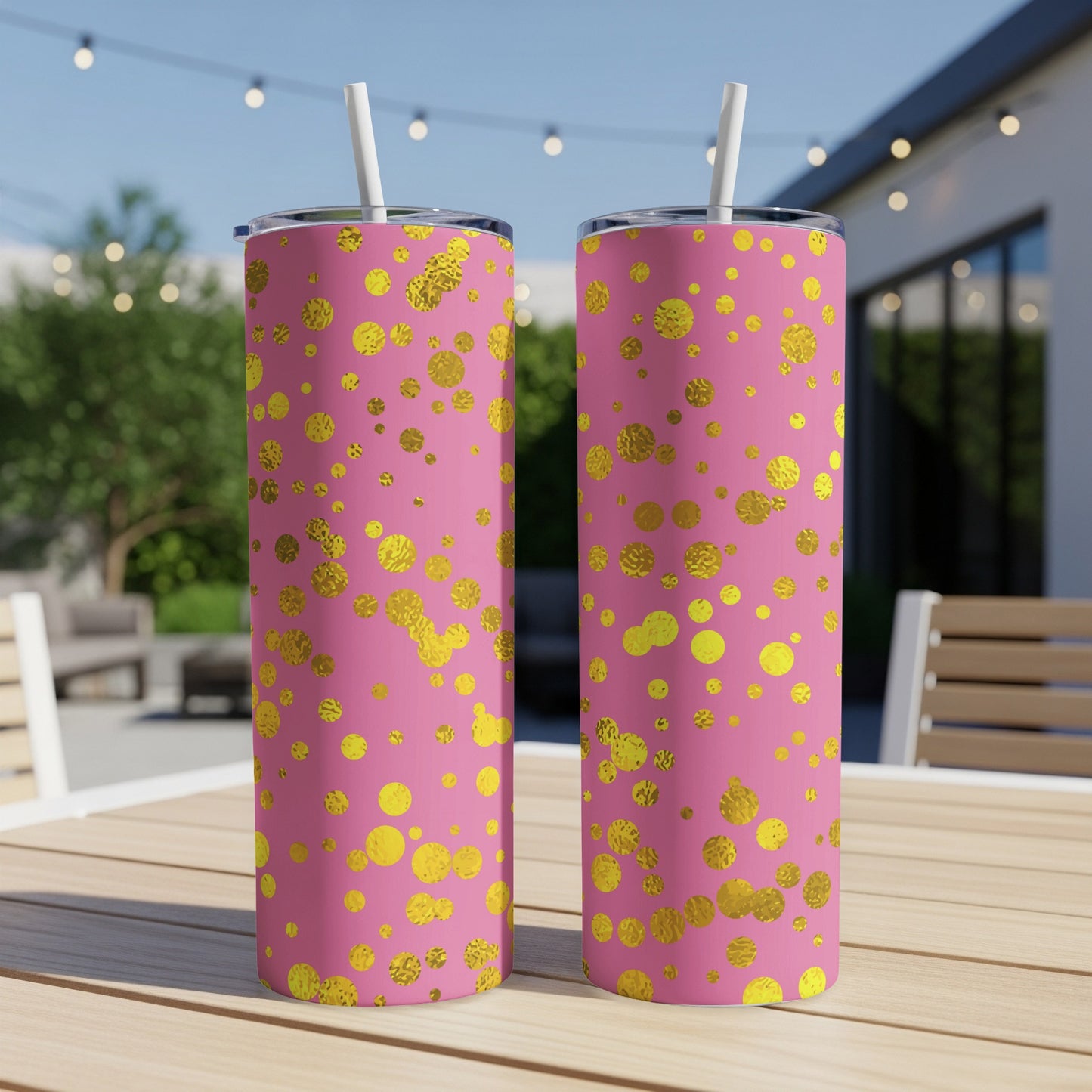 Two pink tumblers with scattered gold dots and white straws on a wooden table.