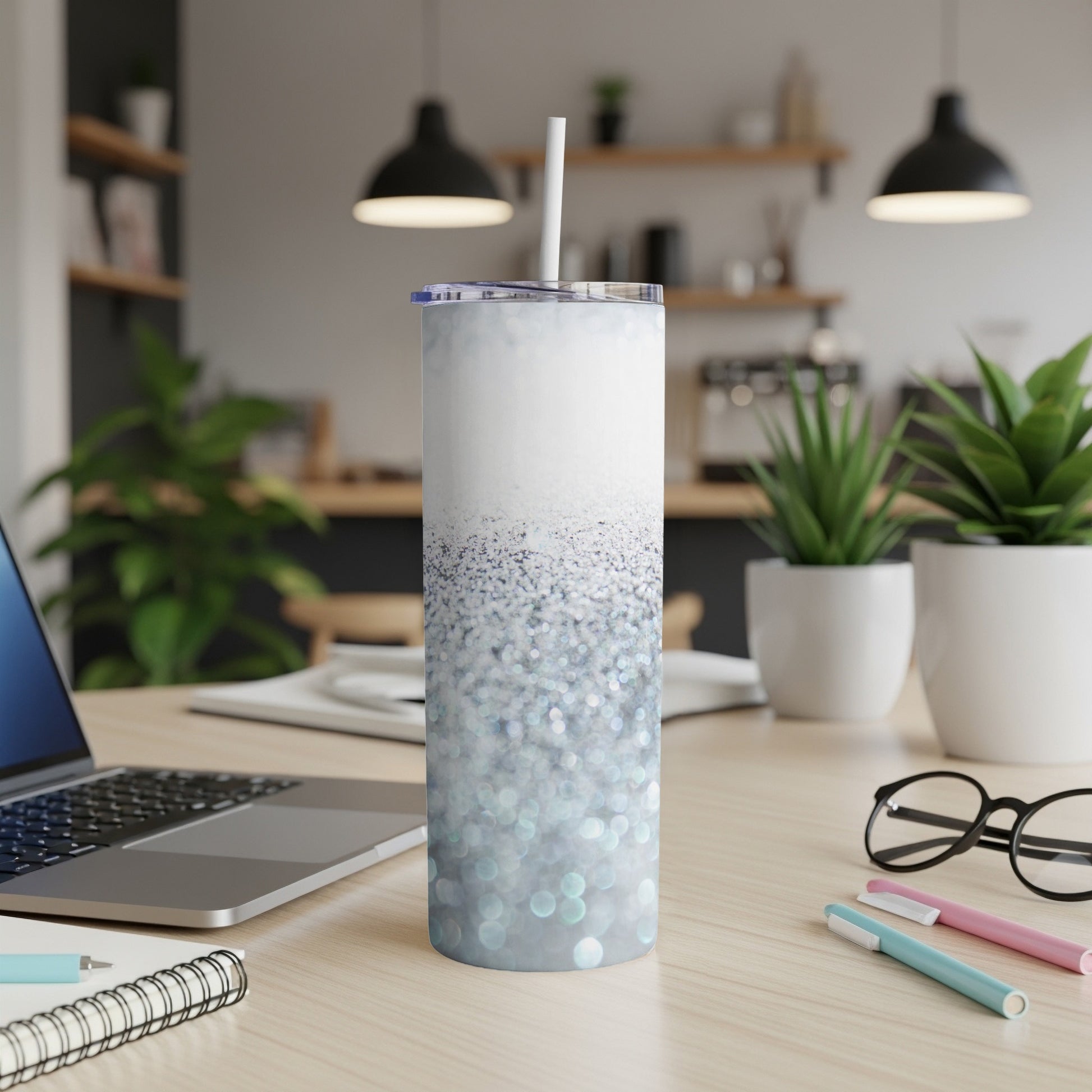 White tumbler with blue glitter, straw, and desk background.
