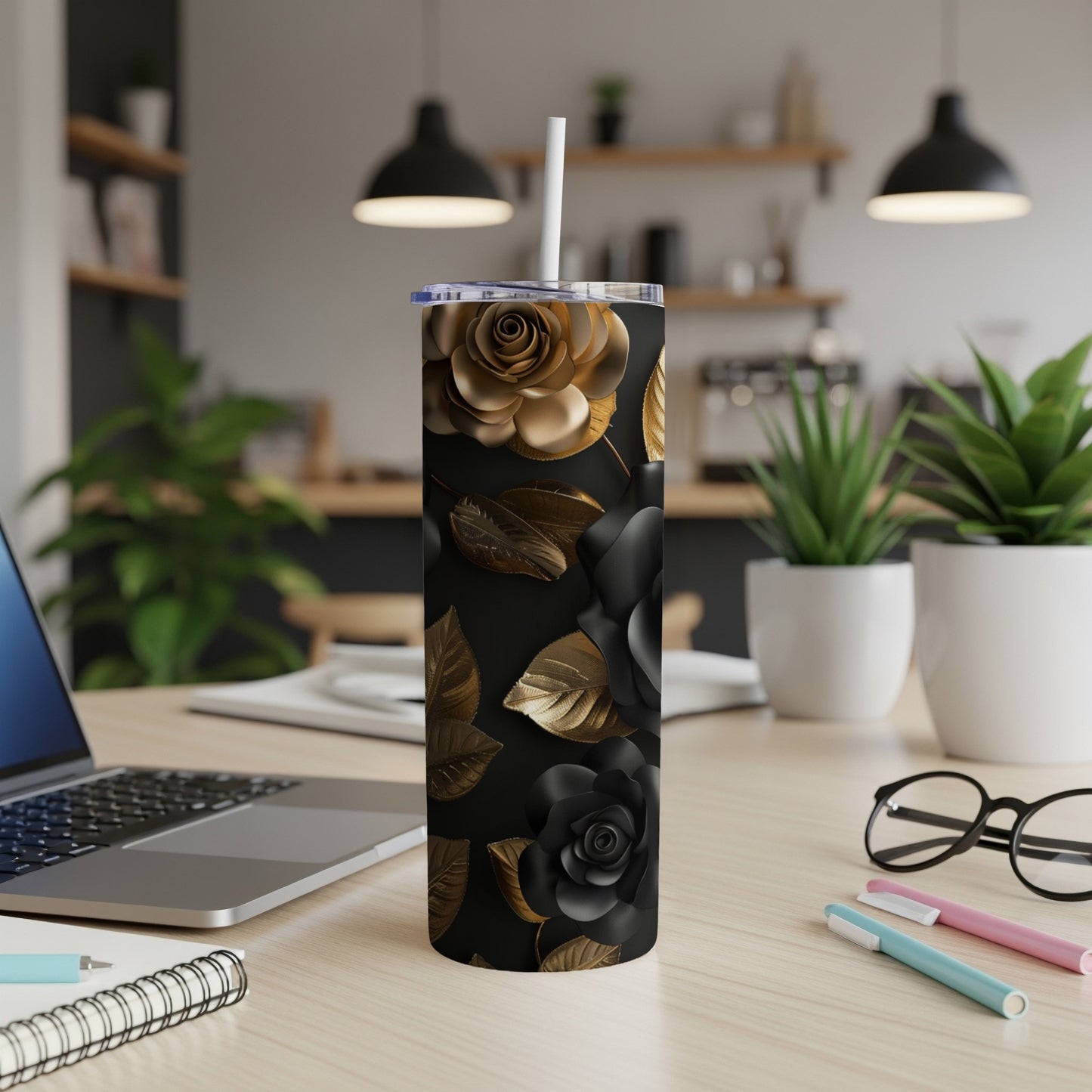 Black tumbler with gold floral design, on a desk with laptop.