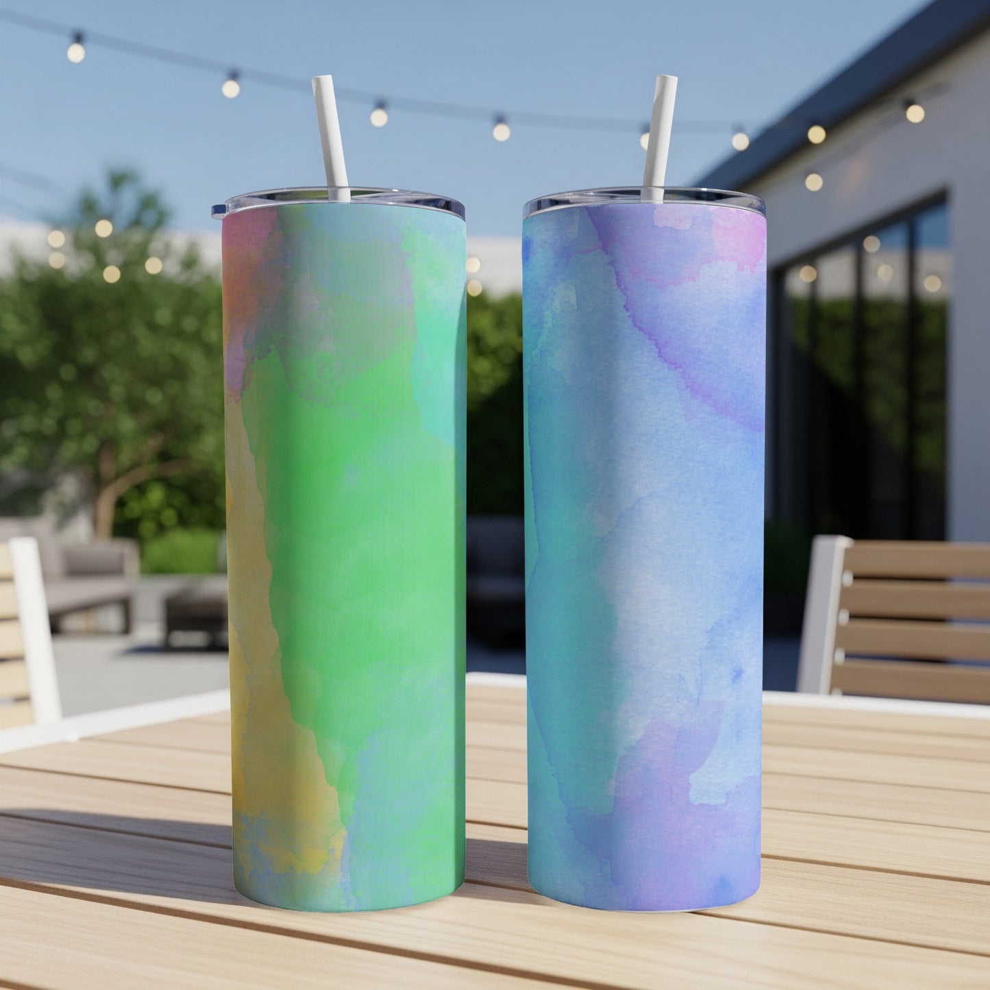 Two tumblers with watercolor designs on a wooden table outdoors.
