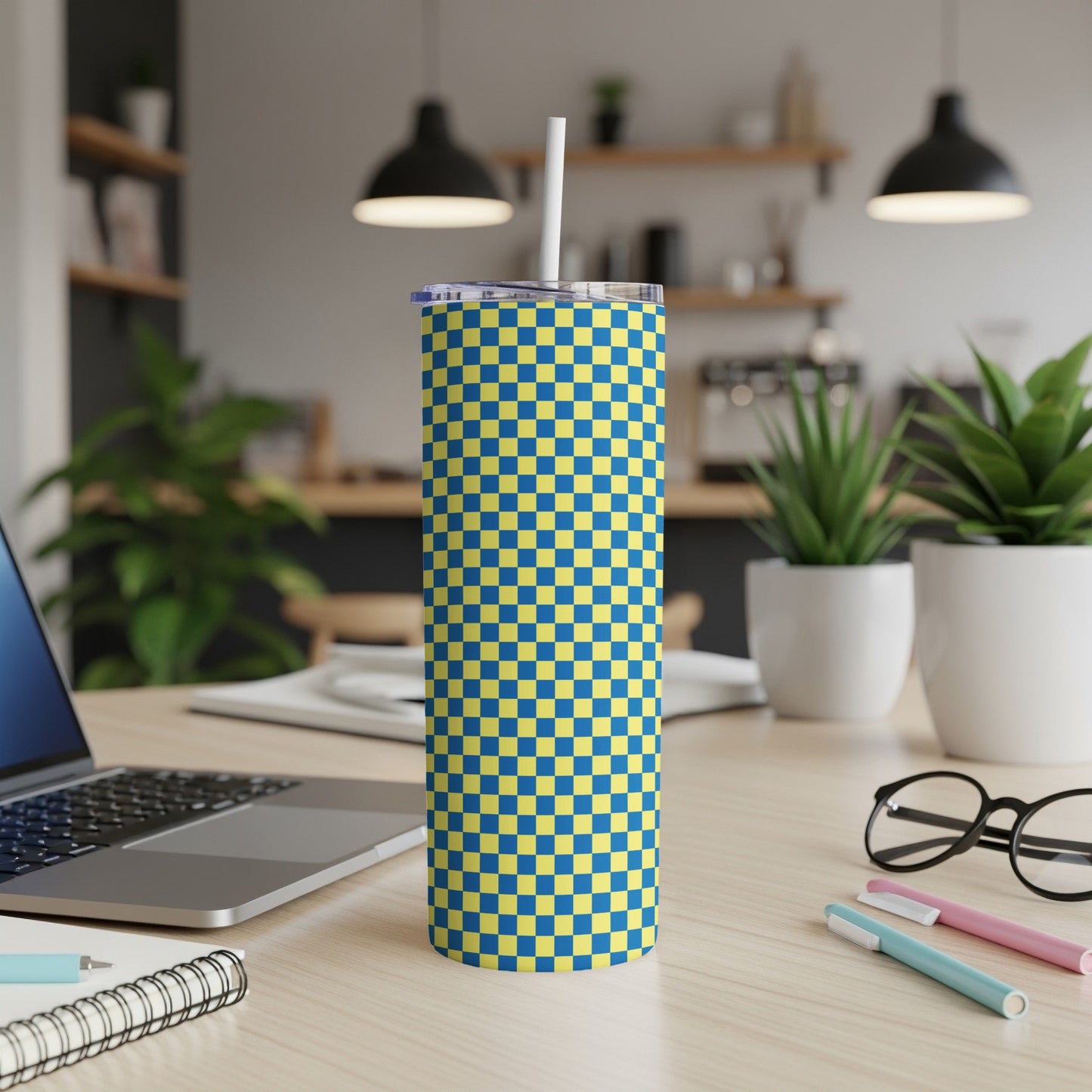 Blue and yellow checkered tumbler with straw on desk.