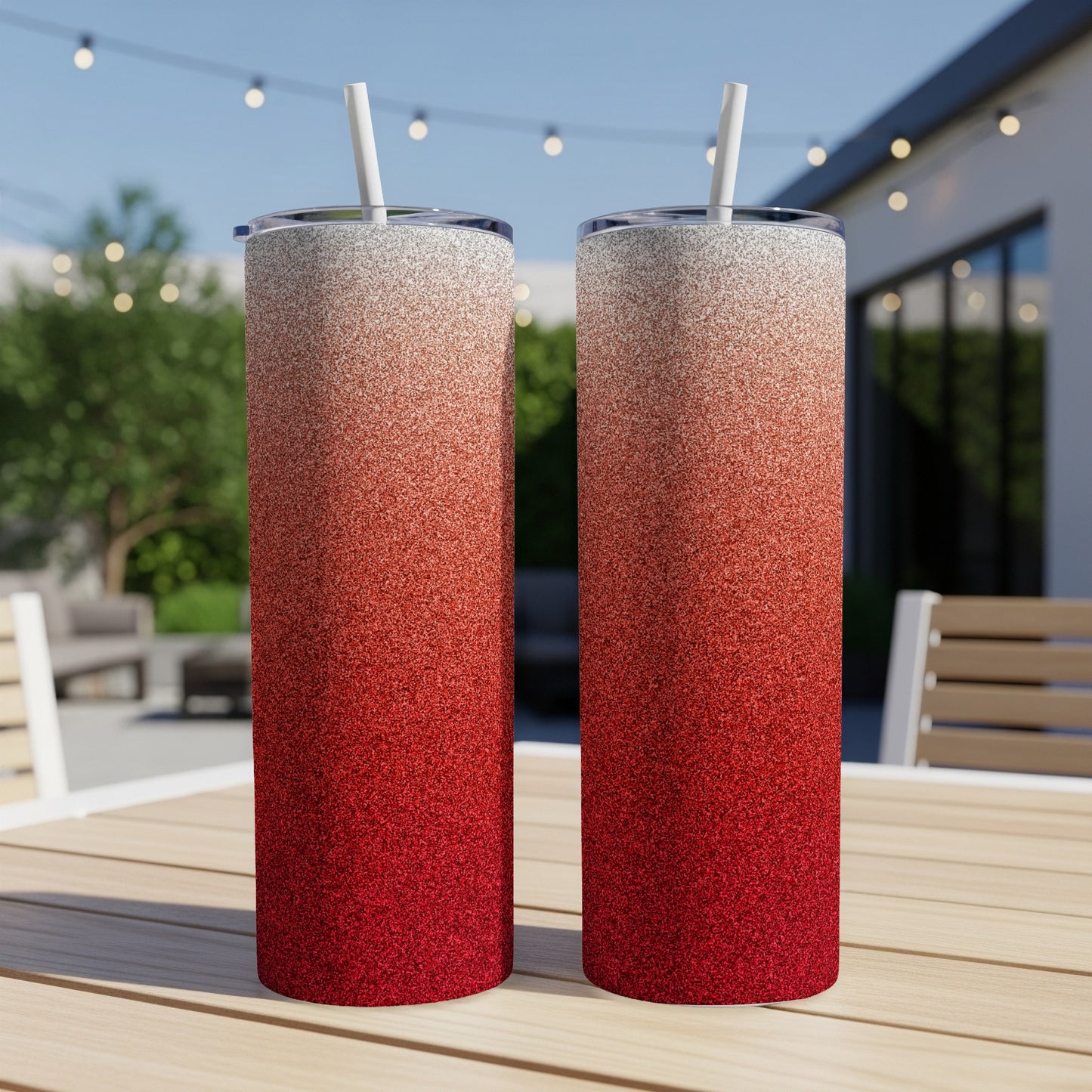 Two tall tumblers with red to white glitter gradient and straws on a table.