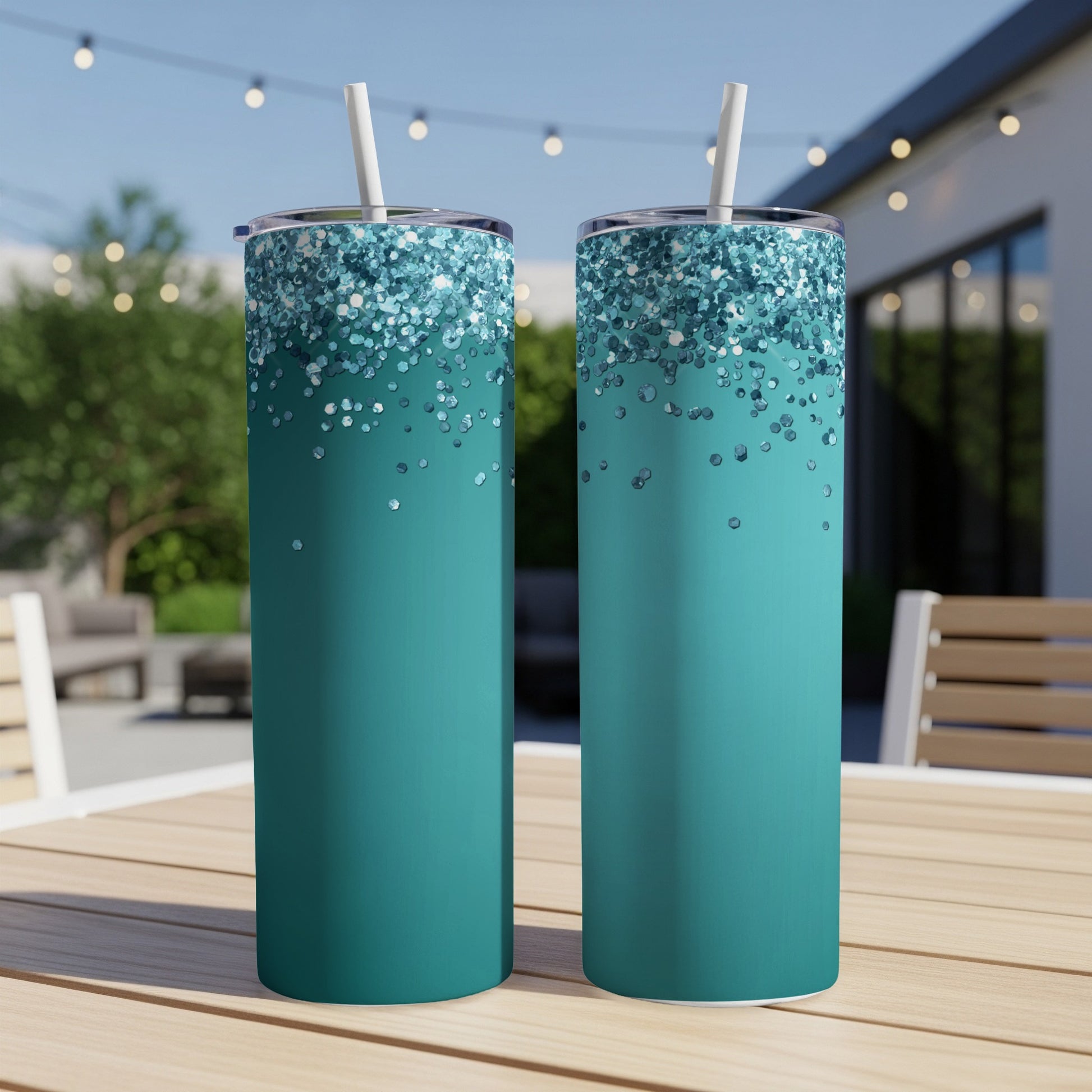 Two teal colored tumblers with glitter accents and white straws stand on a wooden table.