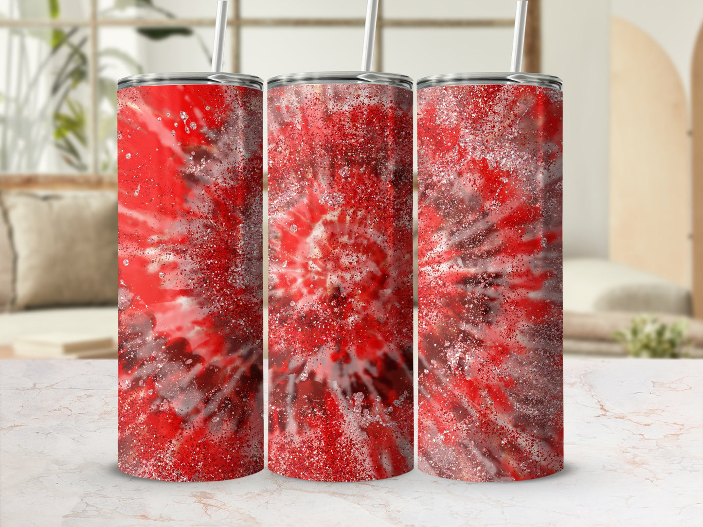 Three red tie-dye tumblers with glitter accents on a white marble surface.