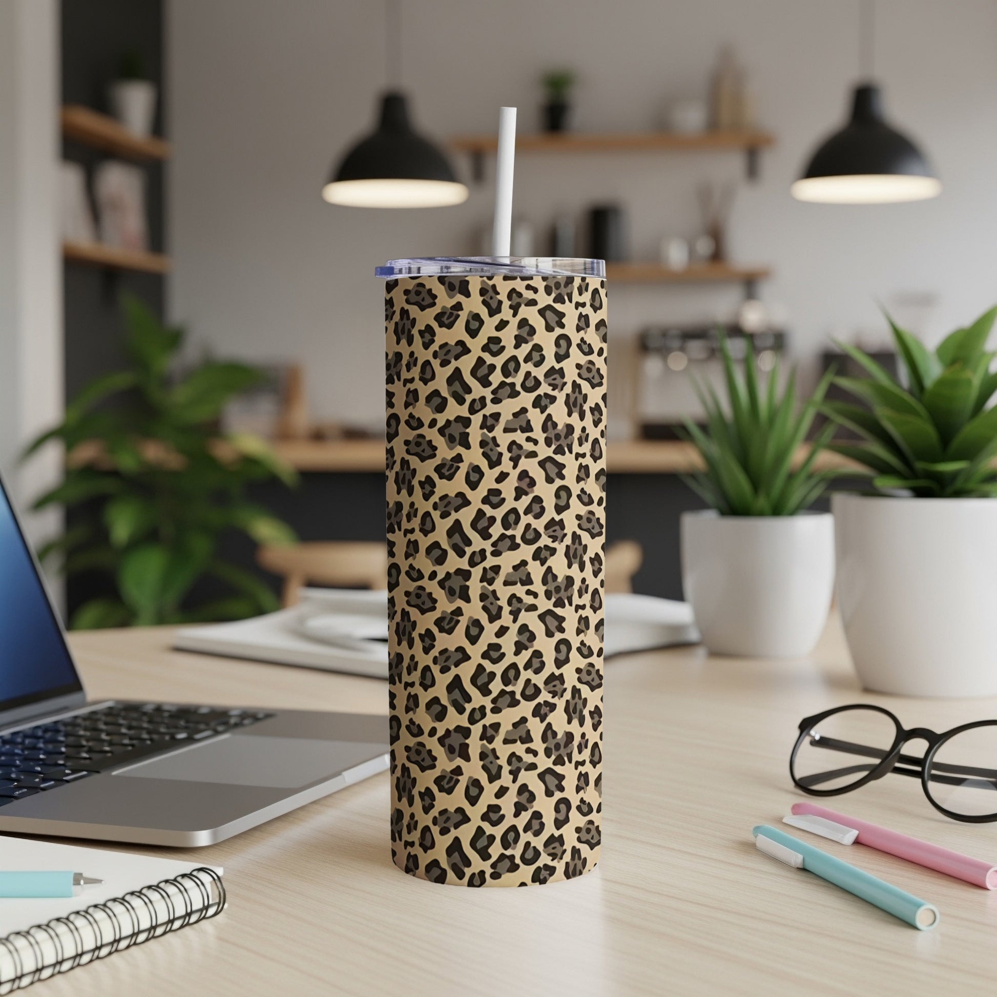 Leopard print tumbler with straw on a desk with laptop and pens.