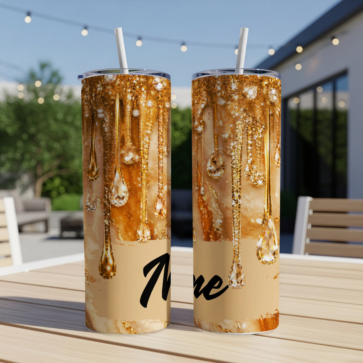 Two gold glitter dripping effect tumblers with straws on a table.