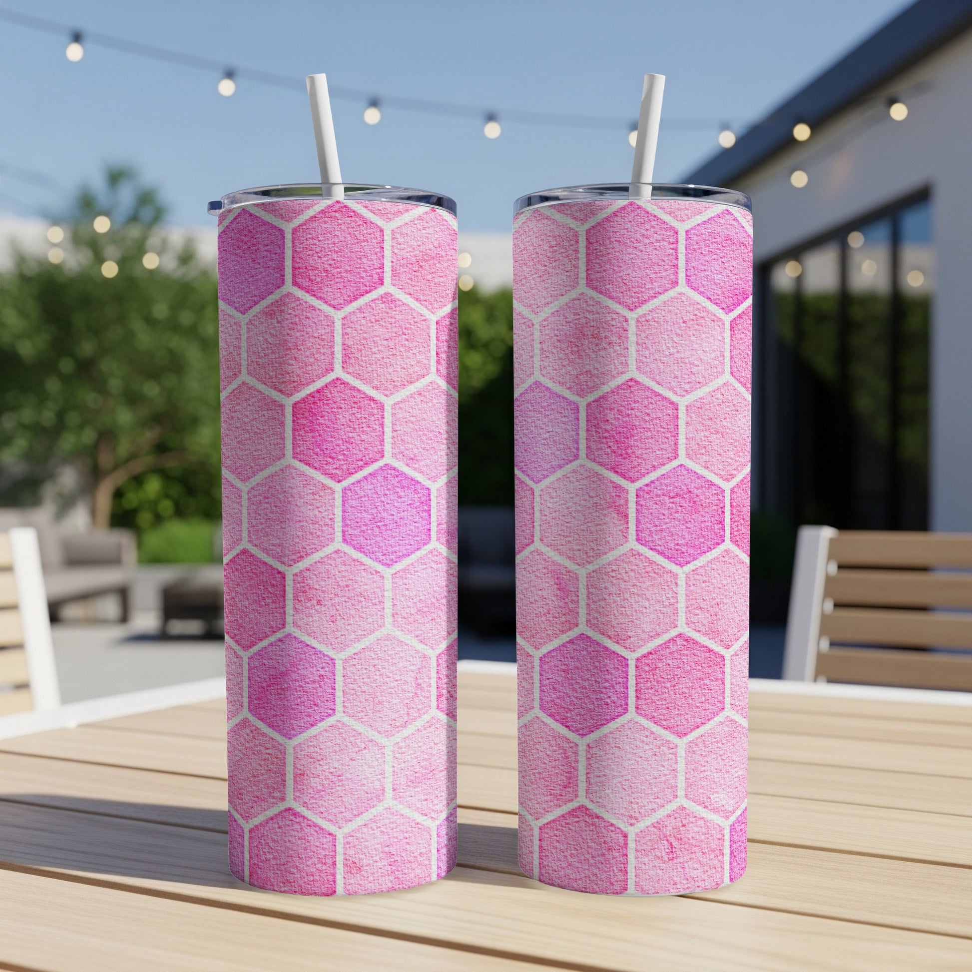 Two pink hexagon pattern tumblers with straws on a wooden table.