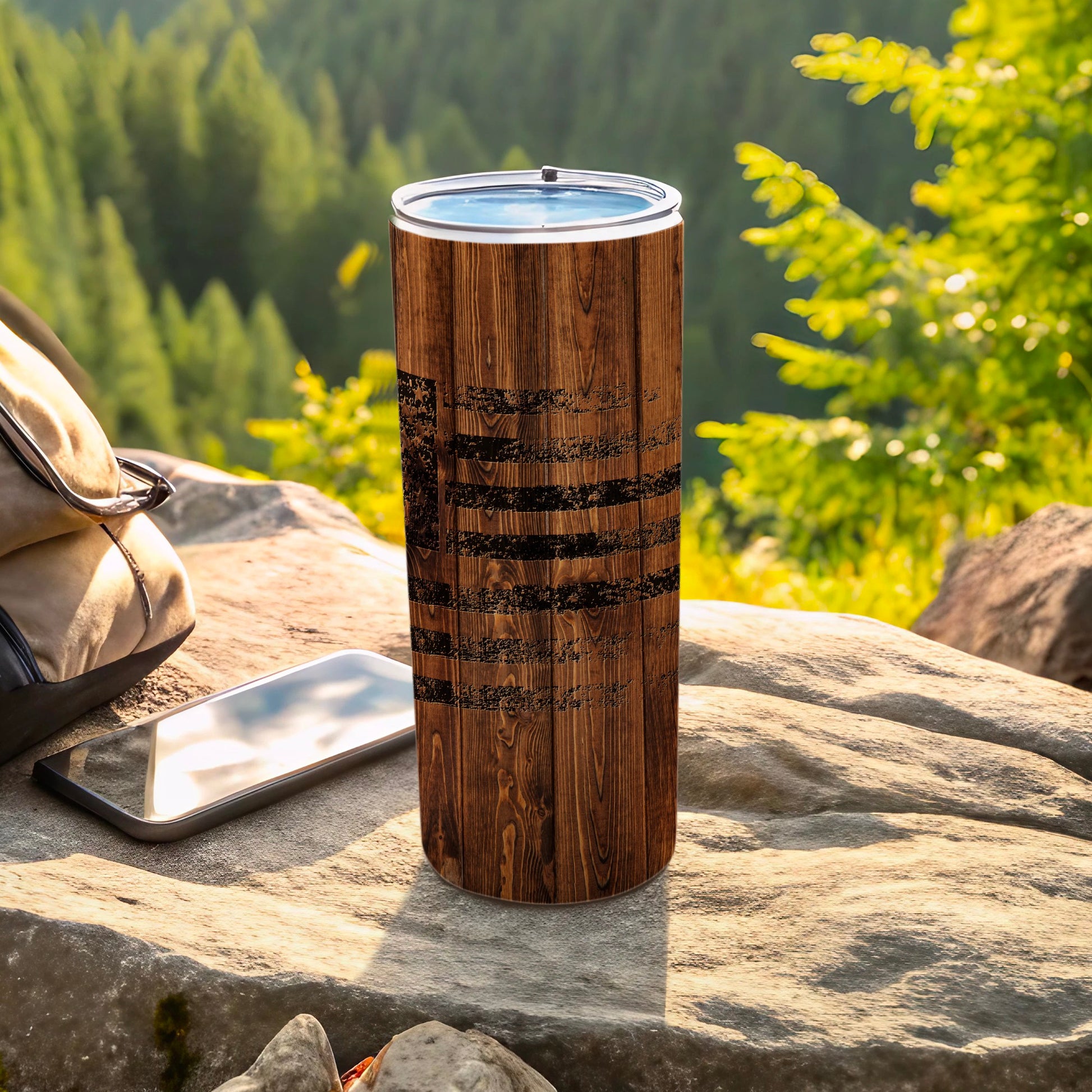 Wooden tumbler with abstract black design sits on rock with phone and backpack.