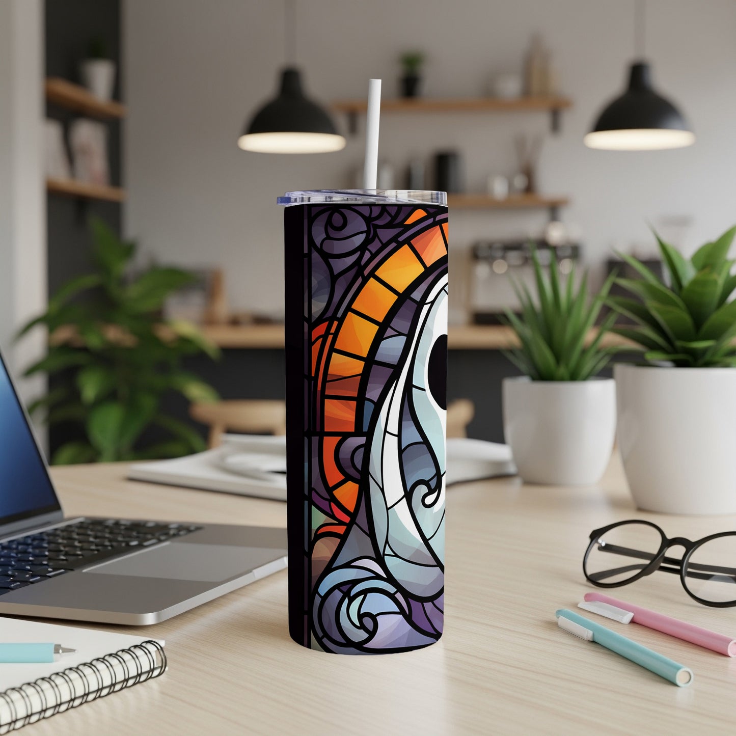 Stained glass tumbler with colorful eye design on desk with laptop and pens.