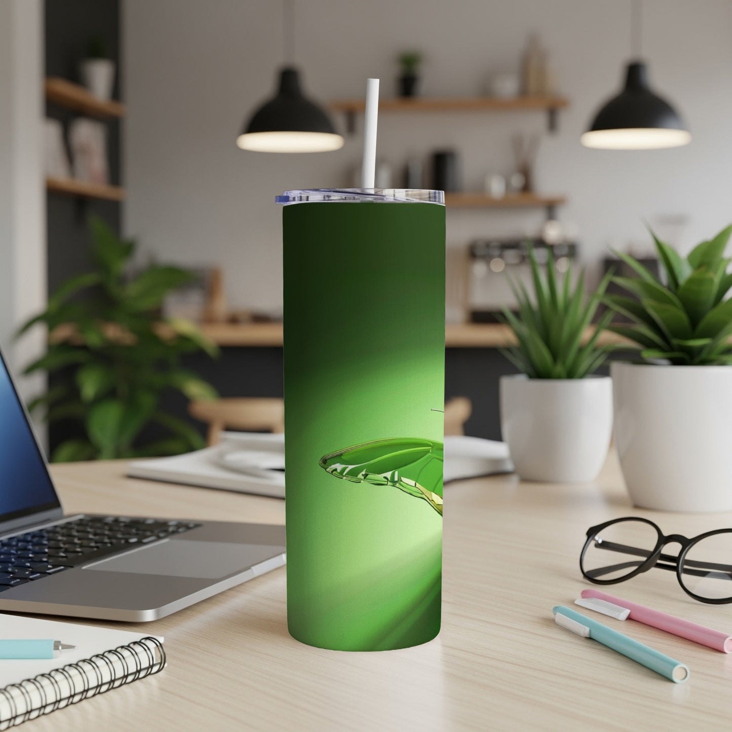 Green metallic tumbler with a dragonfly graphic on a desk.