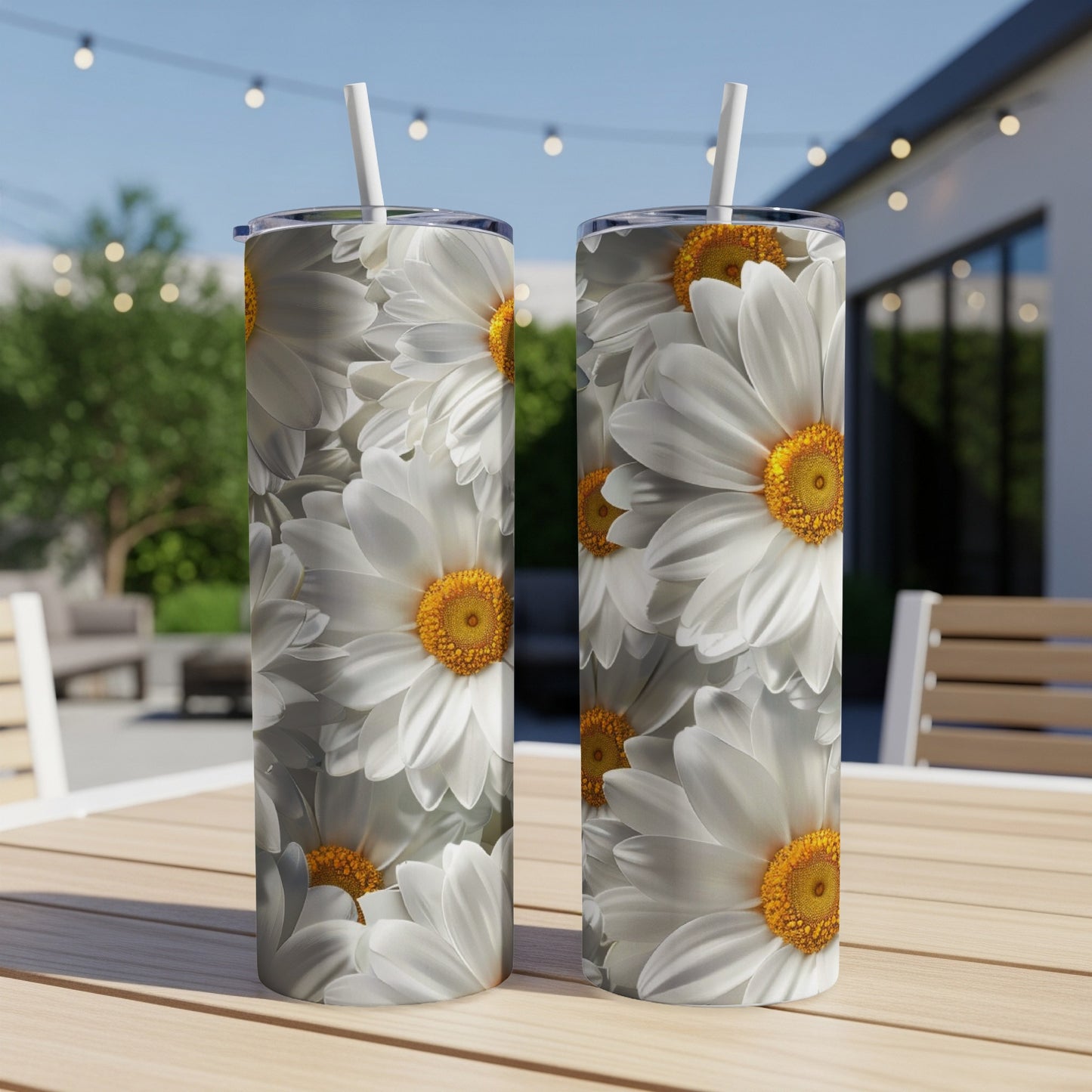 Two tall tumblers with white daisy floral print, with straws, sit on a table.