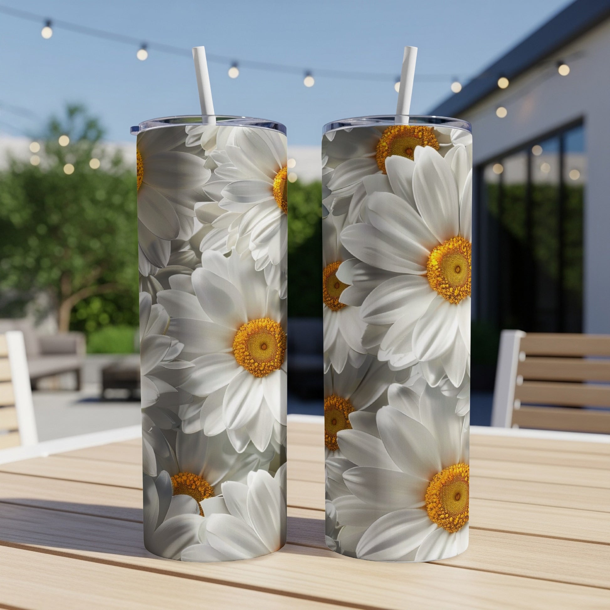 Two tall tumblers with white daisy floral print, with straws, sit on a table.
