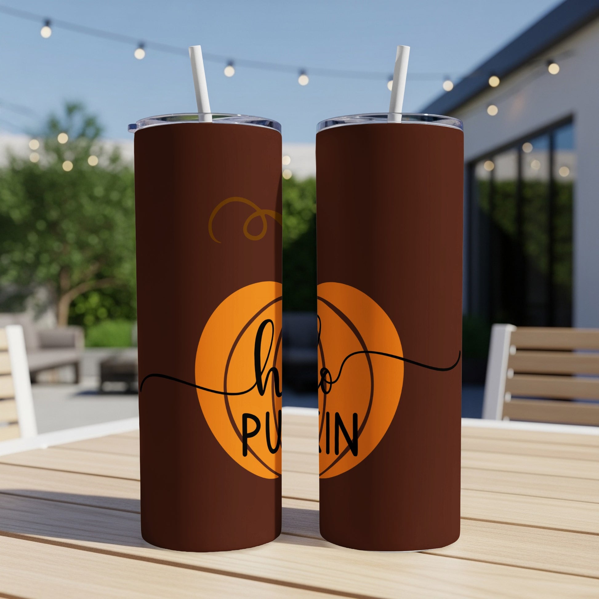 Brown tumbler with "hello pumpkin" graphic, two straws, on outdoor table.