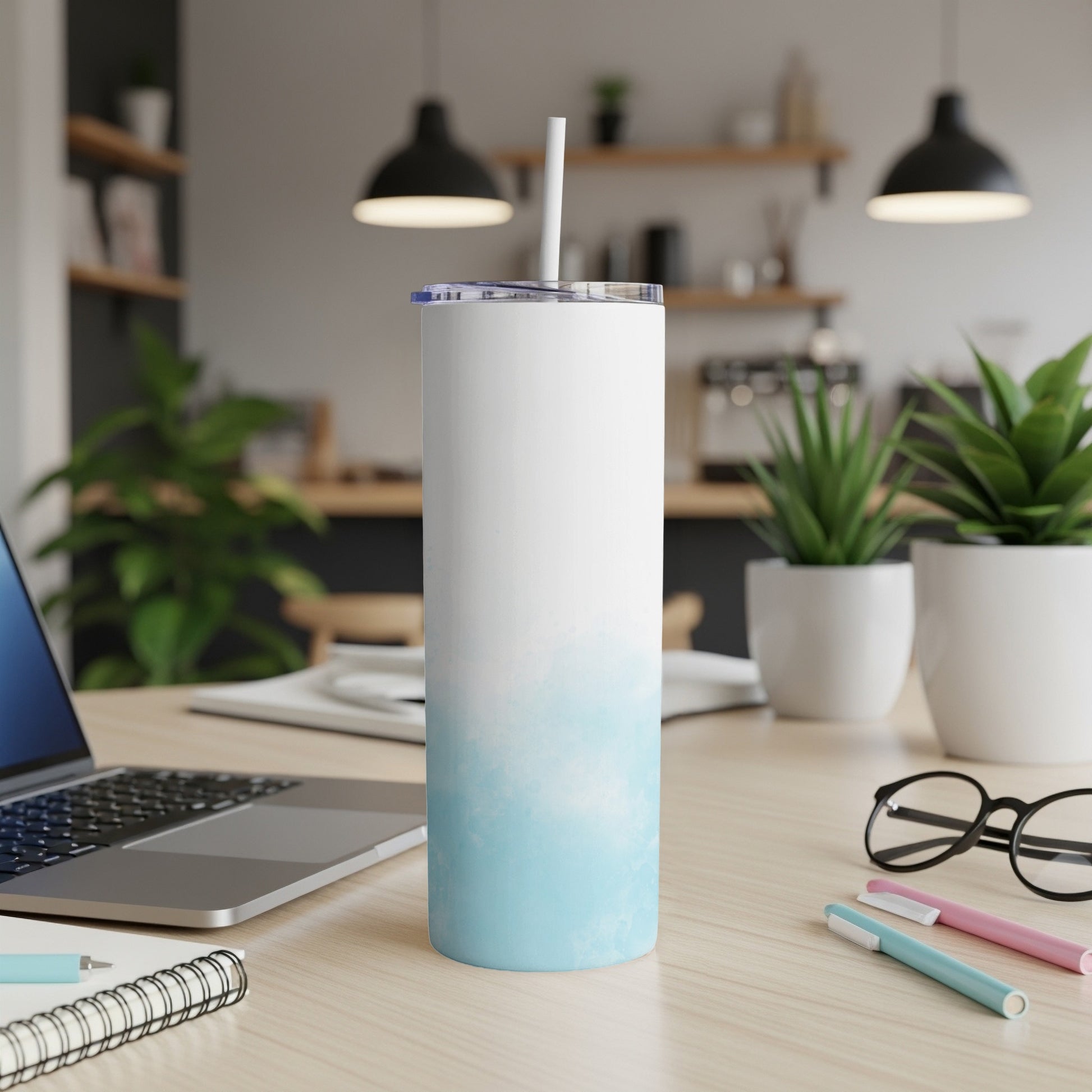 White and blue gradient tumbler with straw on a desk next to a laptop.