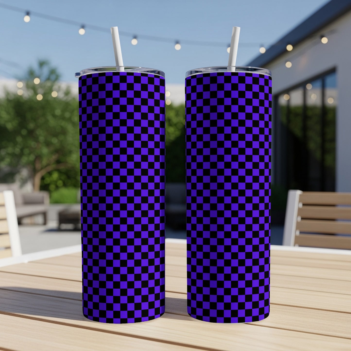 Two purple and black checkered tumblers with straws on a table outdoors.