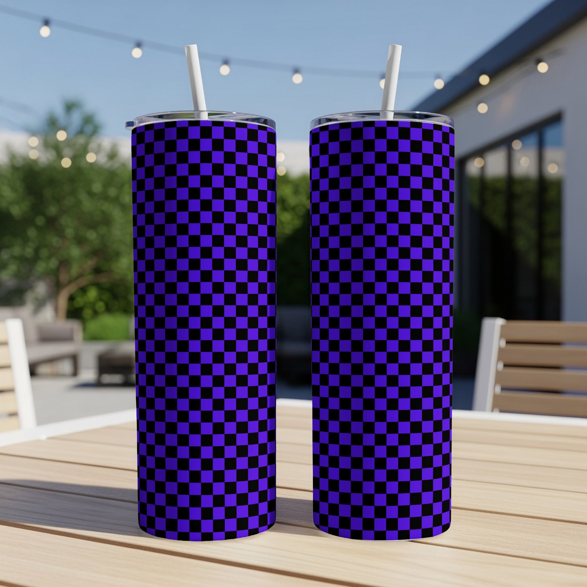 Two purple and black checkered tumblers with straws on a table outdoors.