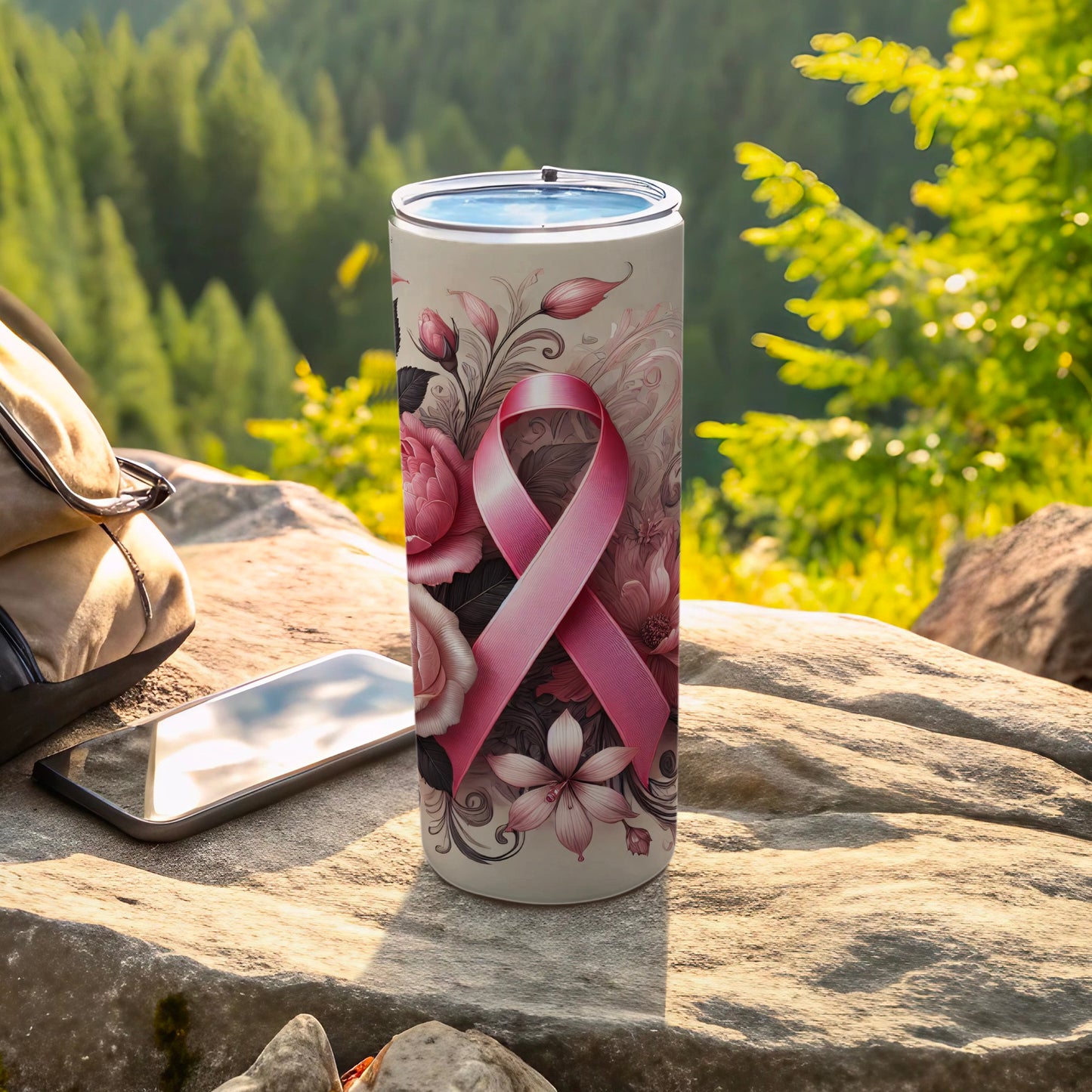 White tumbler with pink ribbon and floral design on rocky outcrop.
