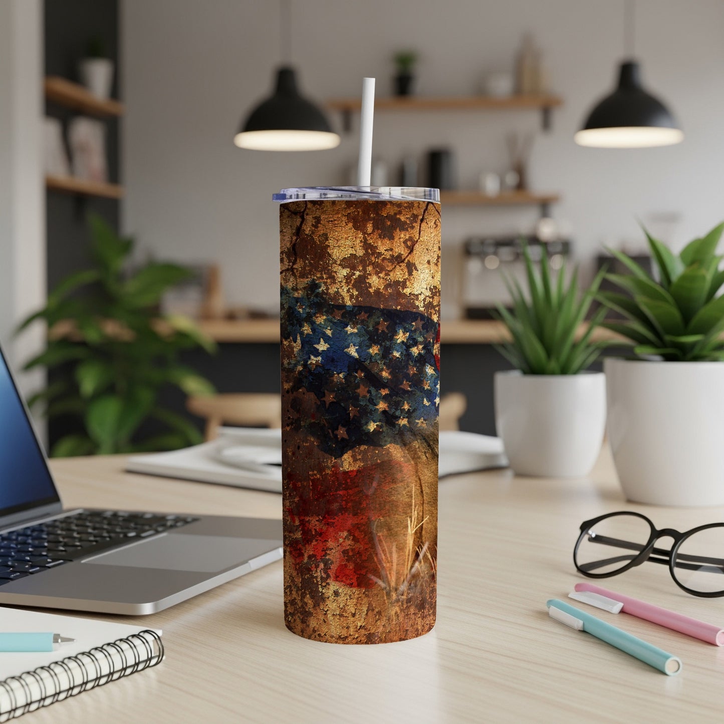 Tall tumbler with distressed American flag design and straw, on desk.