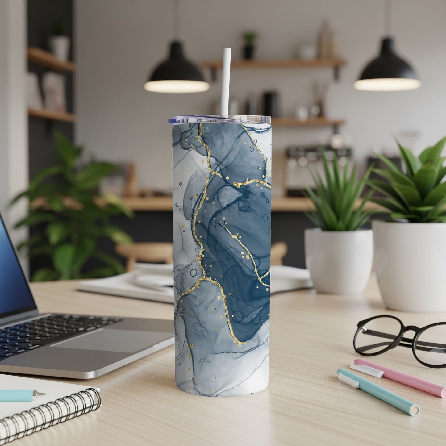 Blue and gold abstract marble pattern tumbler with straw on desk.