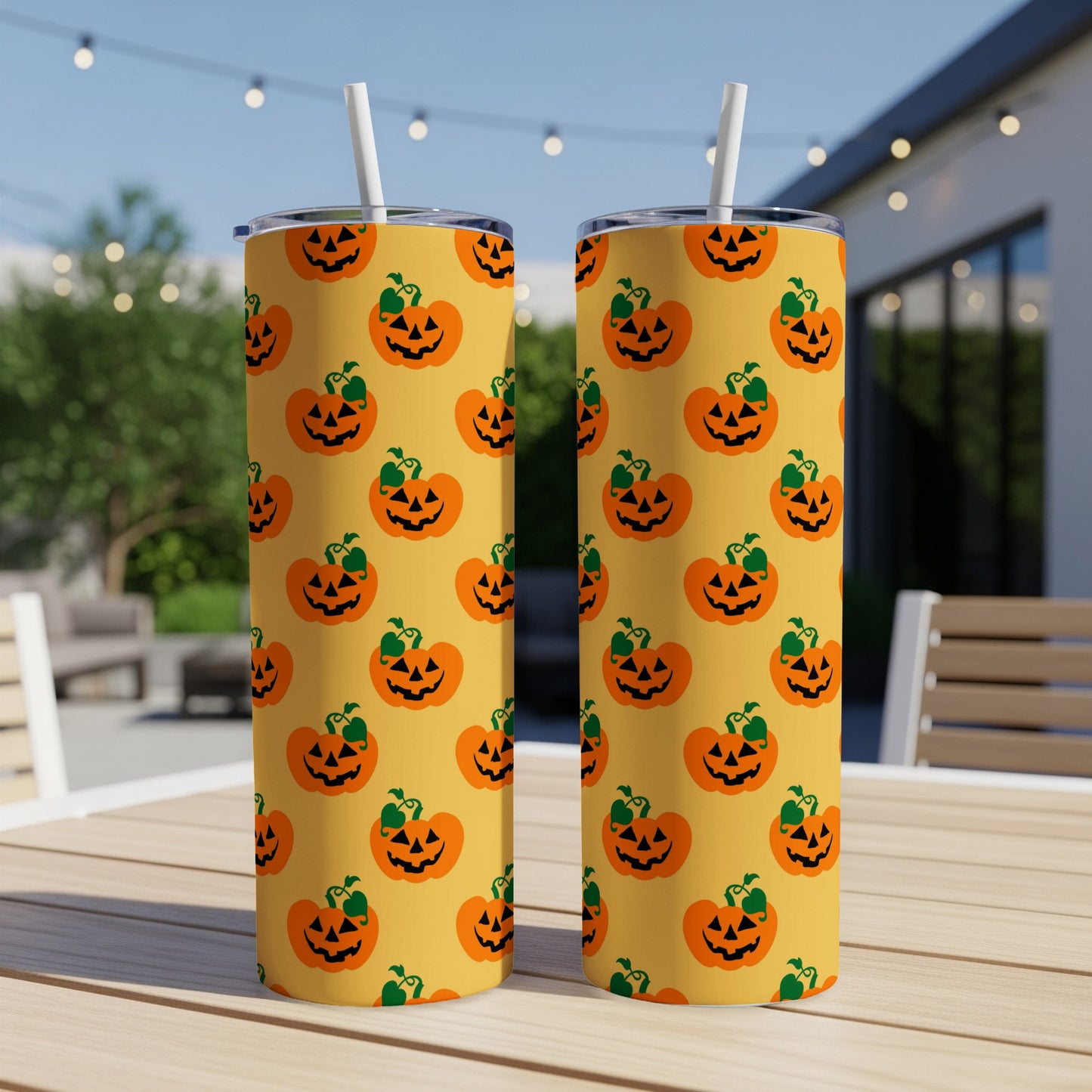 Two tumblers with a repeating jack-o'-lantern pattern sit on a wooden table outdoors.