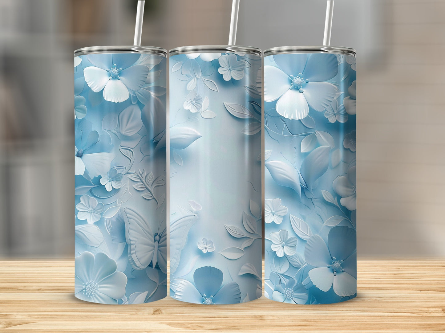 Three blue floral tumblers with butterfly accents on a wooden surface.