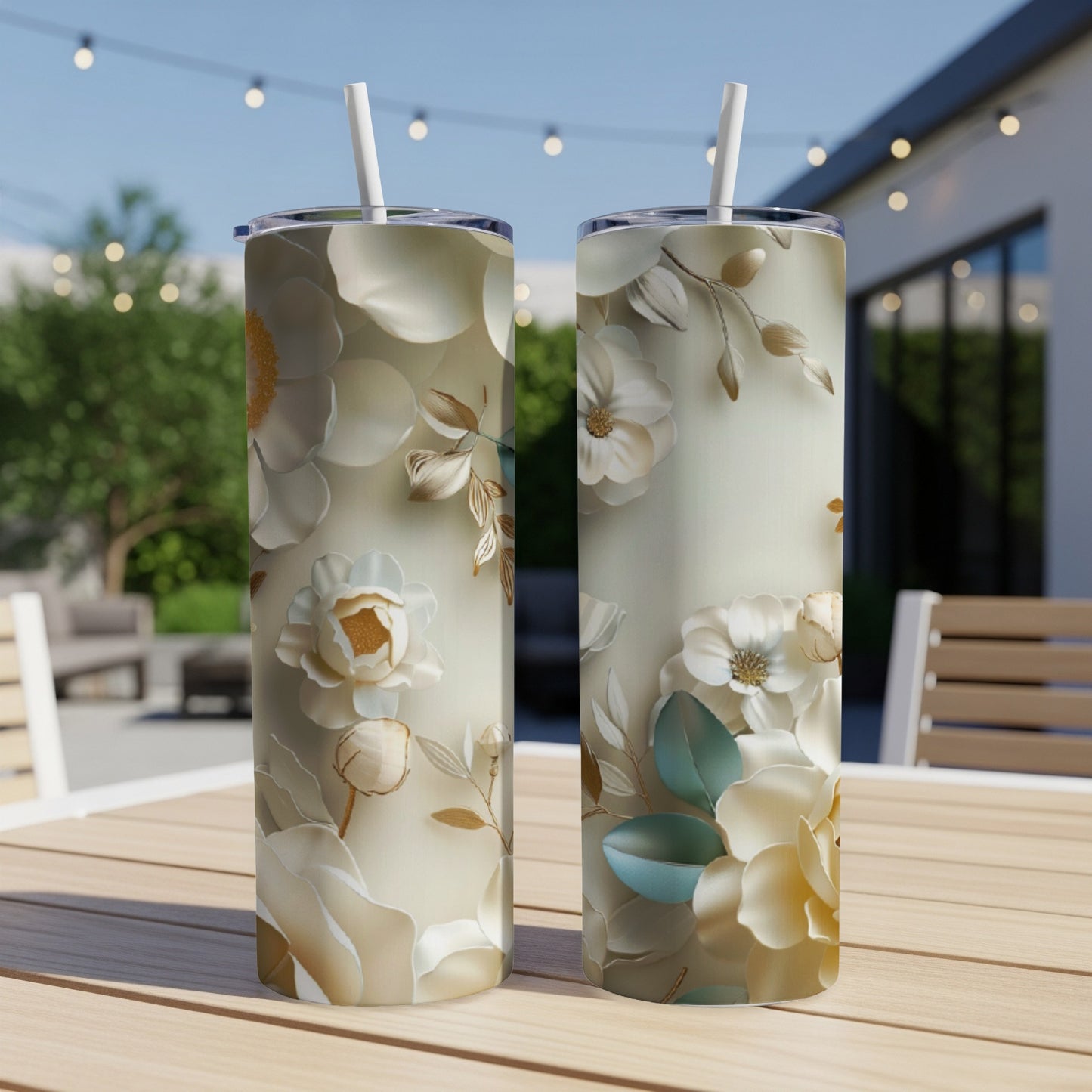 Two floral tumblers with straw on a wooden table outdoors.
