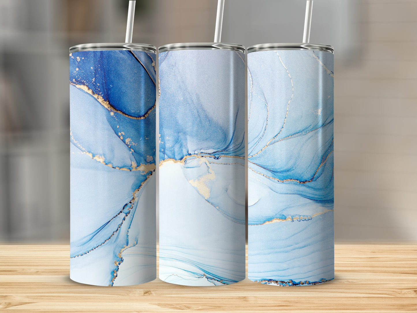 Three tumblers with swirling blue and gold abstract patterns stand on a wooden surface.