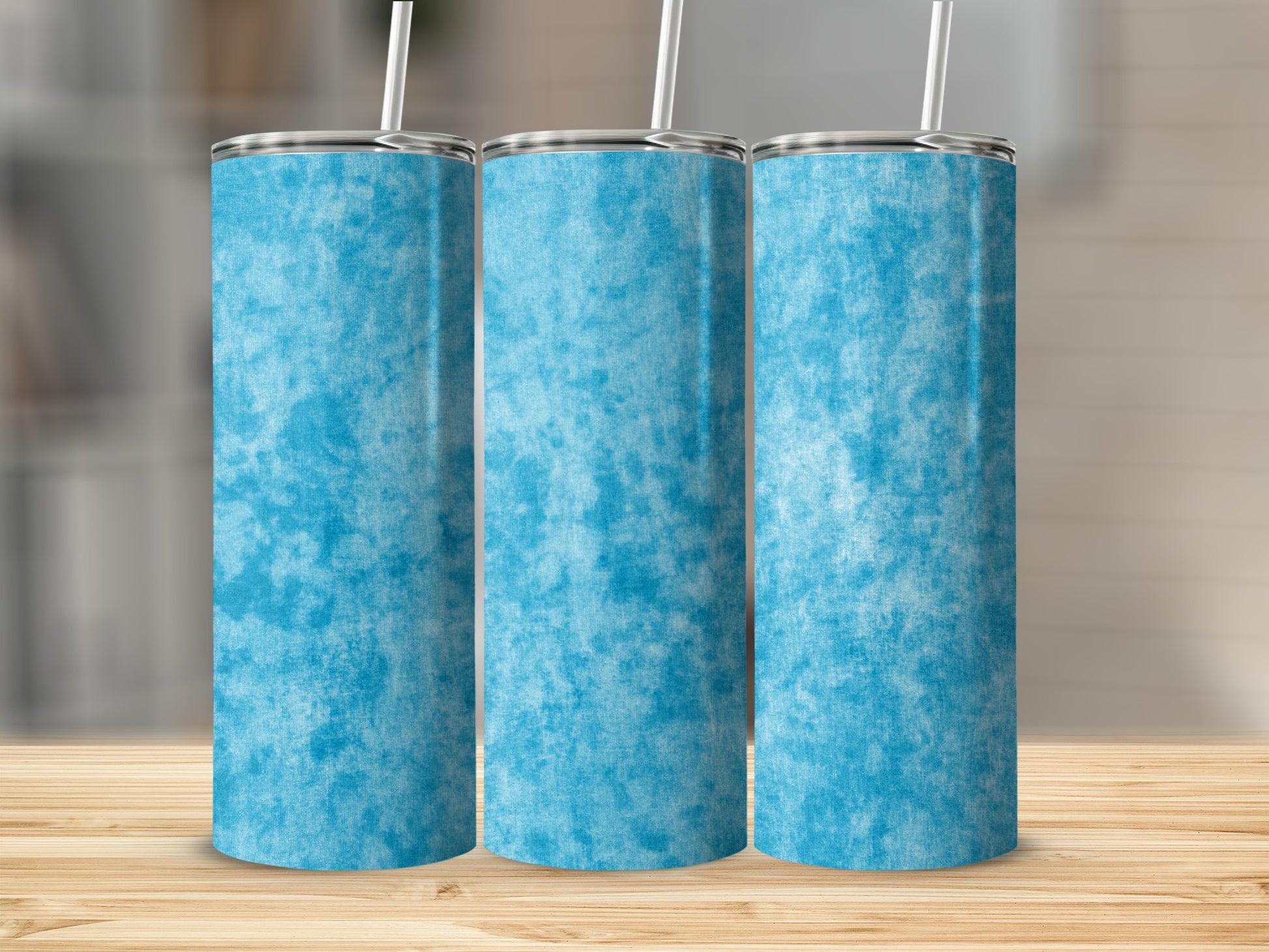 Three blue textured tumblers with straws stand on a wooden surface.