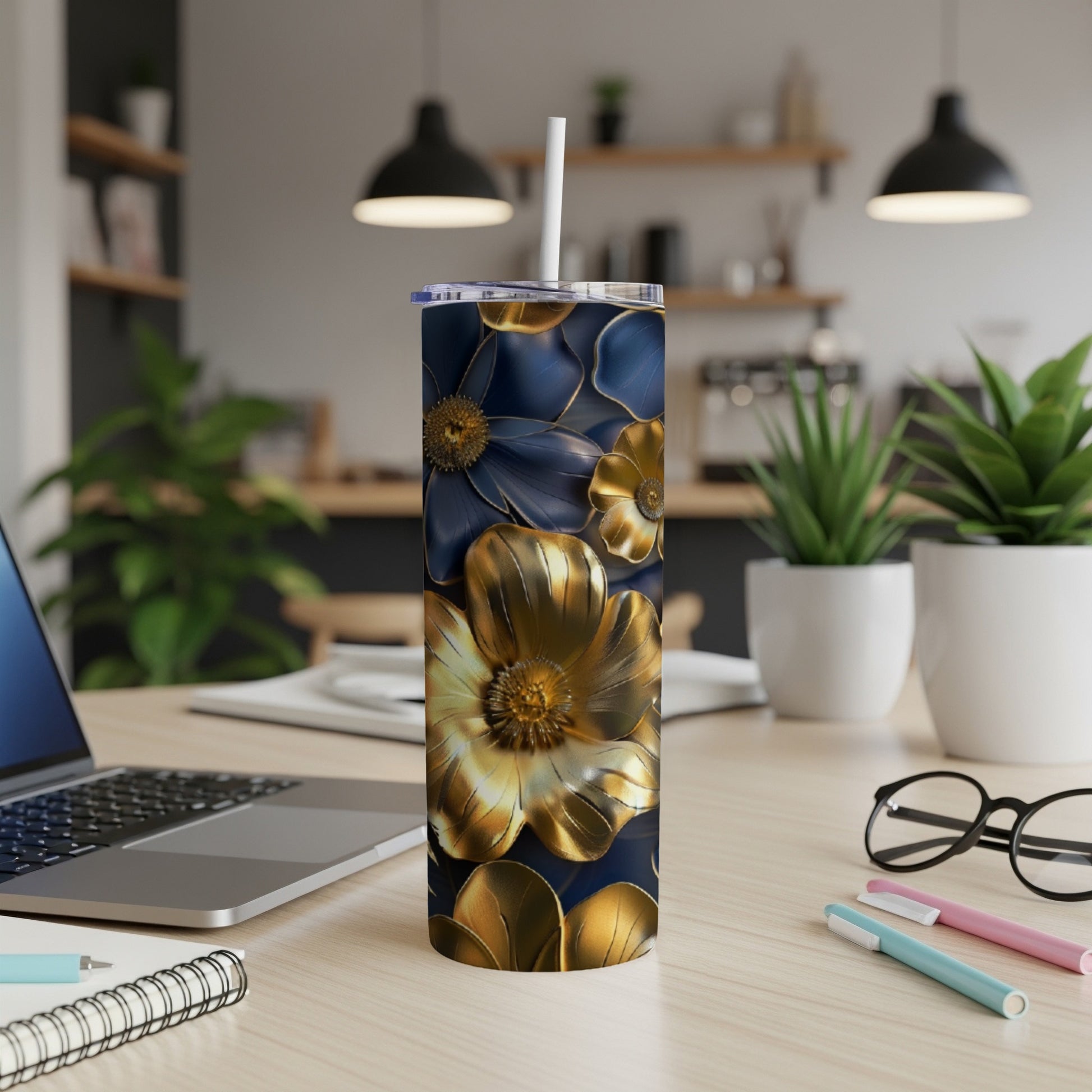 Navy blue tumbler with gold floral design, straw, on a desk.