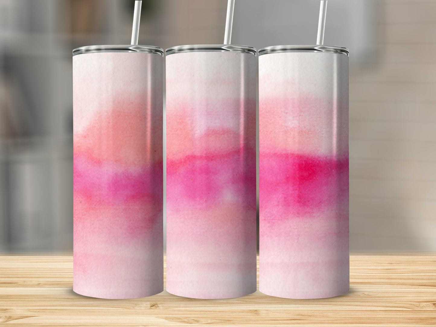 Three pink and white watercolor tumblers with straws on a wooden surface.