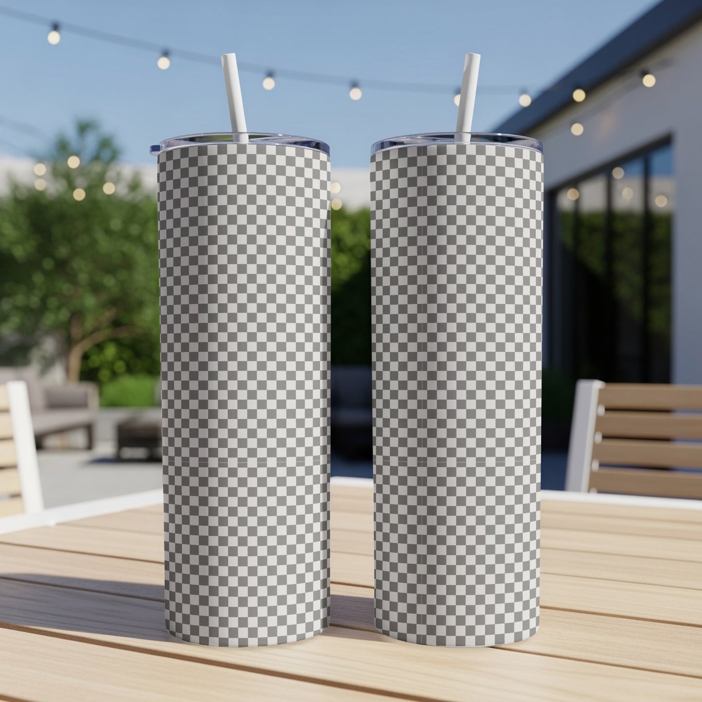 Two tall, checkered tumblers with straws on a wooden table outdoors.