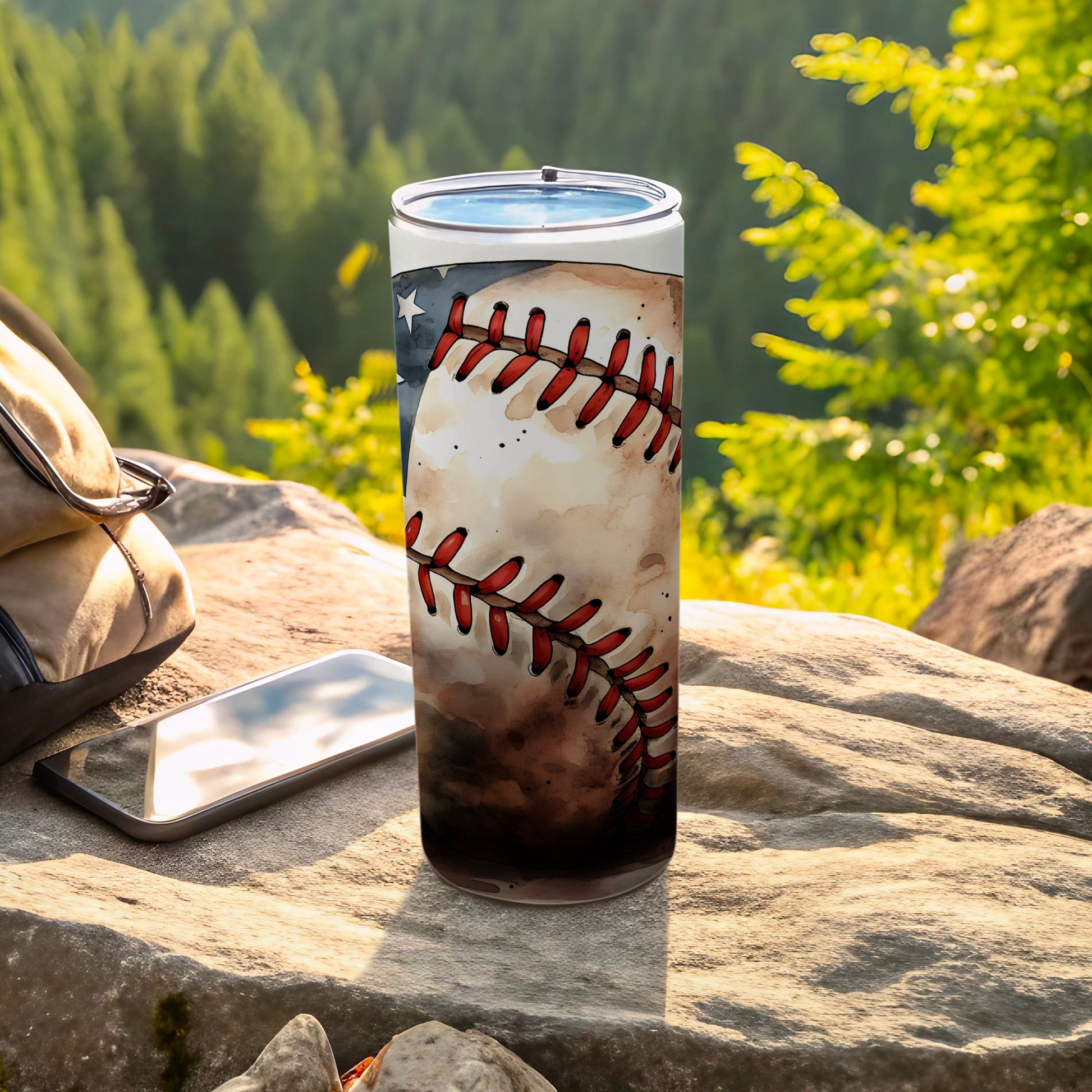 Baseball tumbler with American flag design on rocky outcrop near backpack.