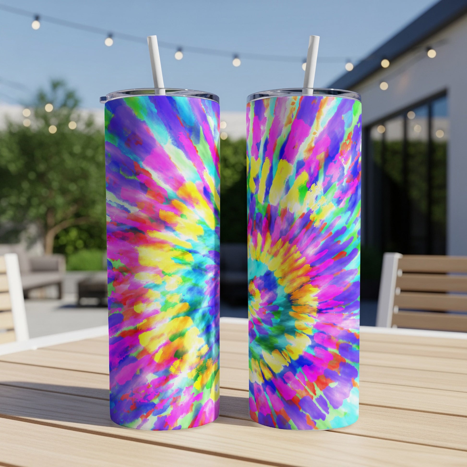 Two tall tumblers with vibrant tie-dye patterns and white straws sit on a wooden table.