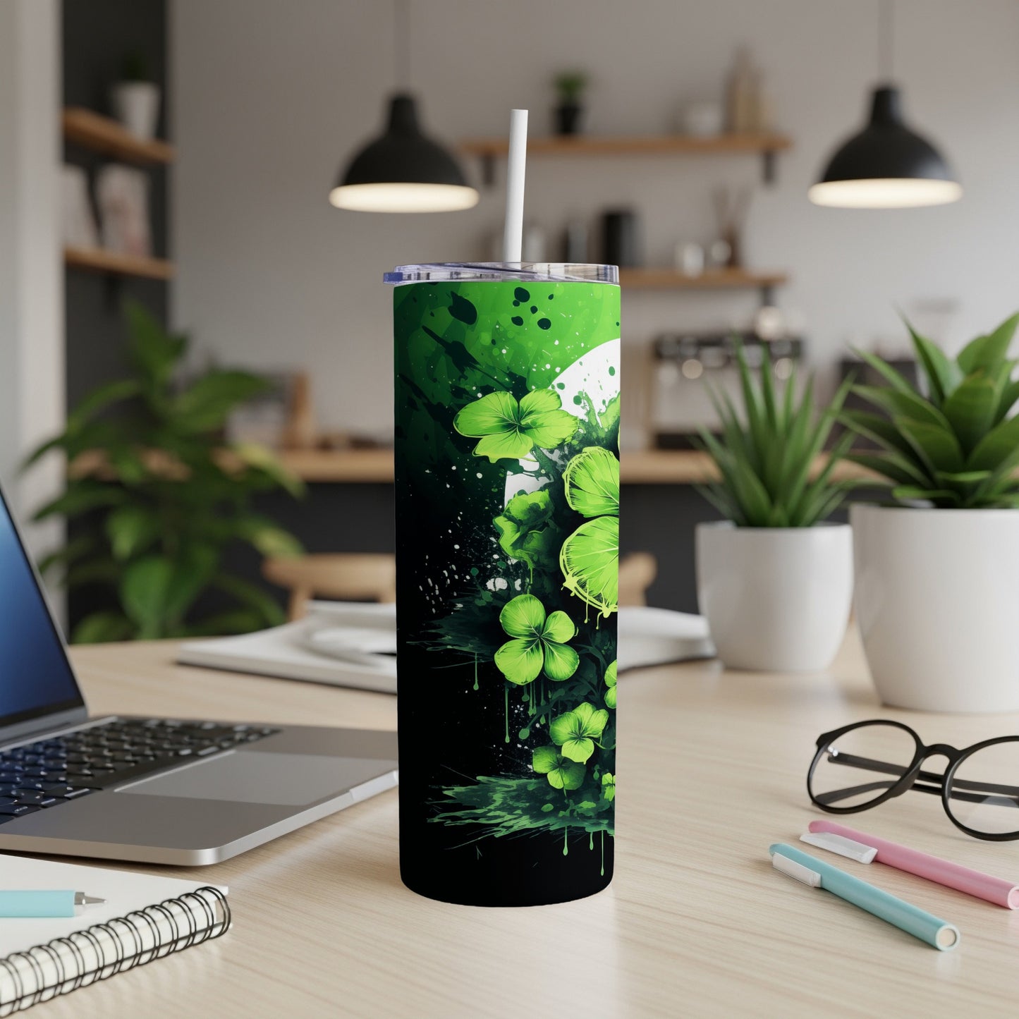Green shamrocks and splatters on a black tumbler with a white straw.