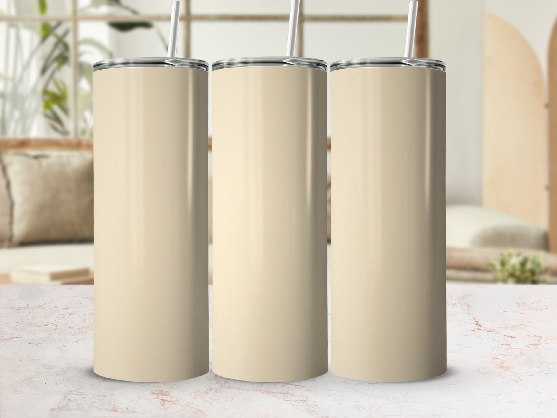 Three cream-colored tumblers with straws on a marble surface.