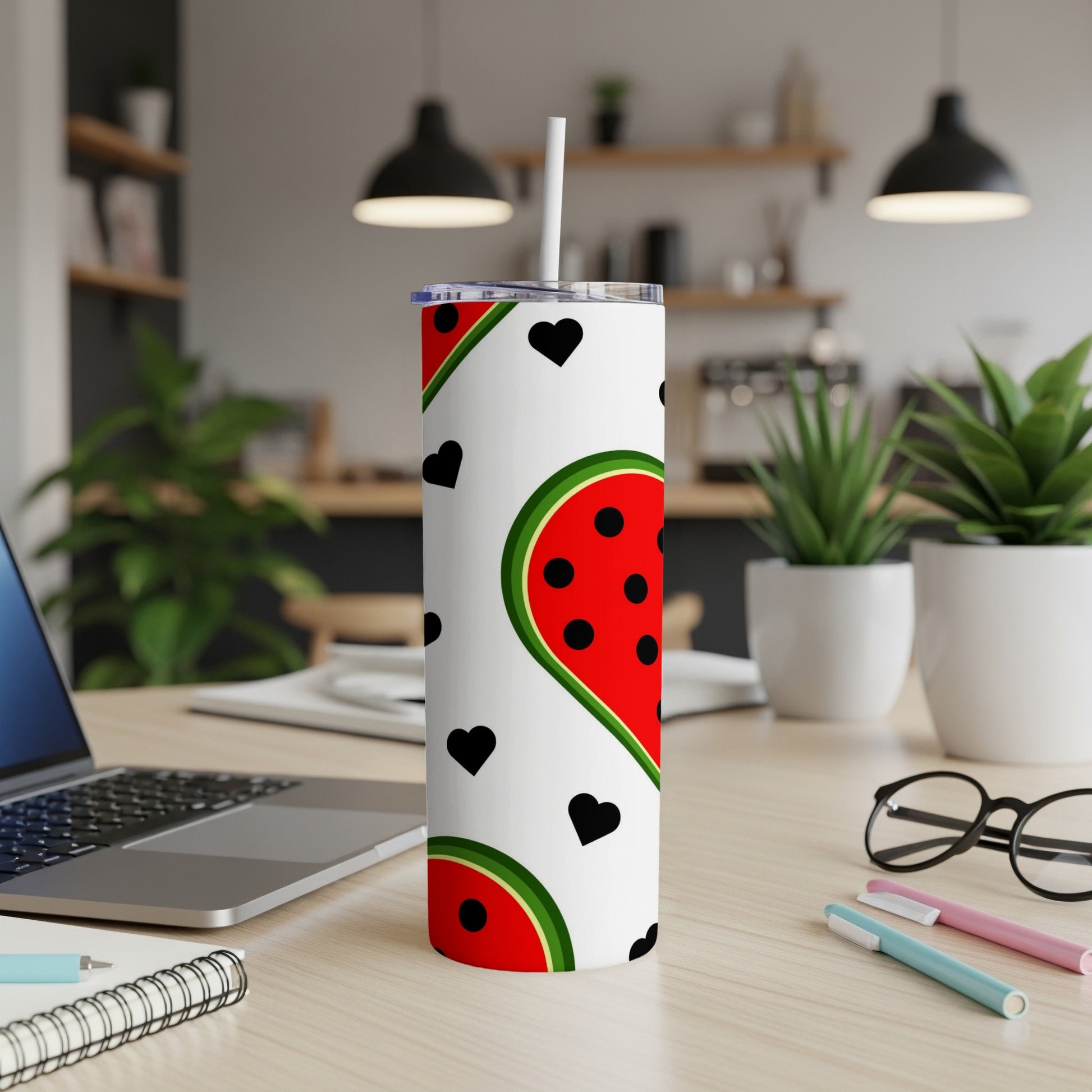 White tumbler with watermelon slices and black hearts, on a desk.