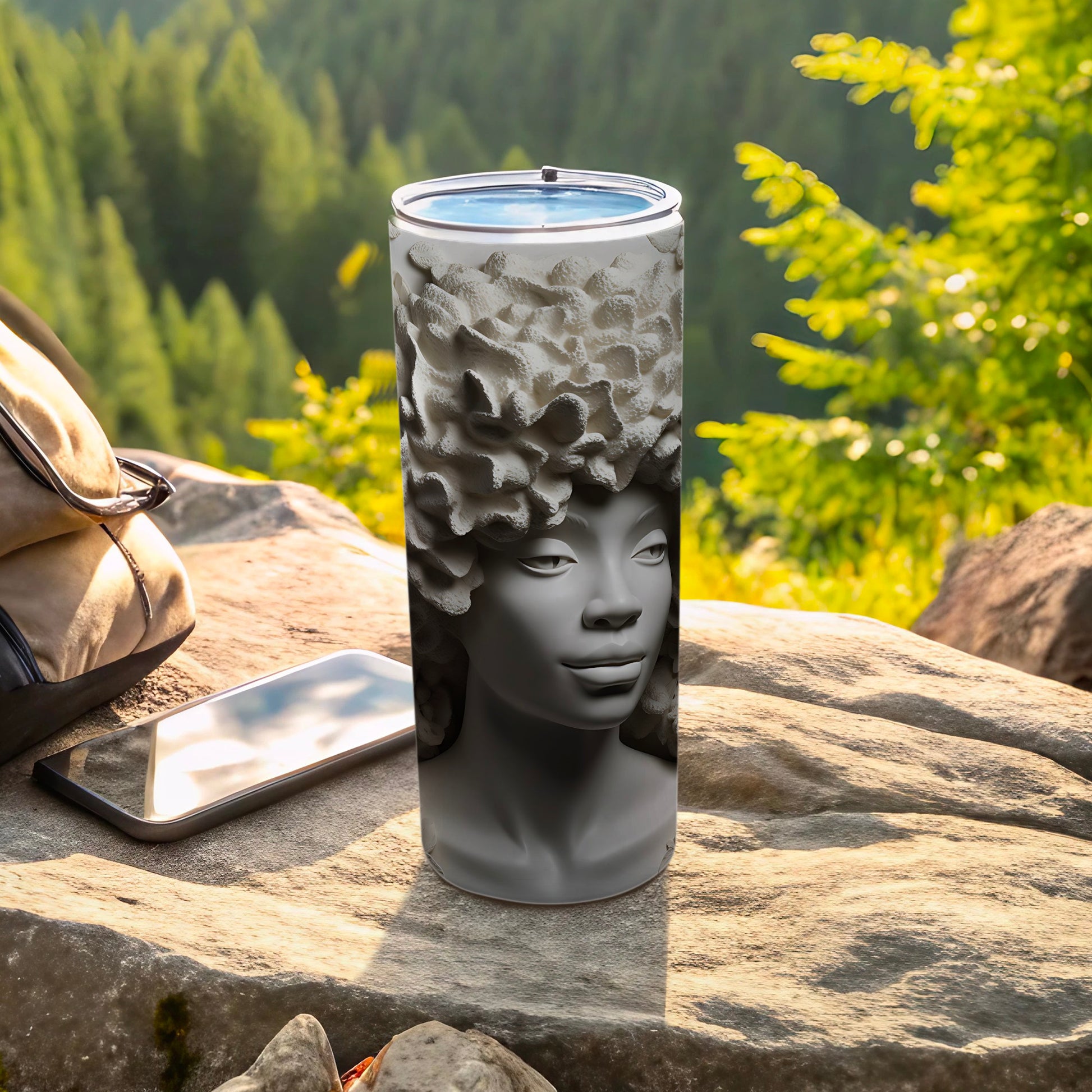 Gray tumbler with textured hair design, outdoors next to phone and bag.