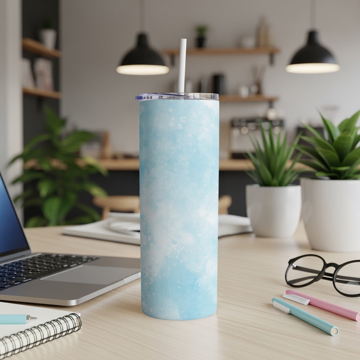 Light blue tie-dye pattern tumbler with straw on a wooden desk.